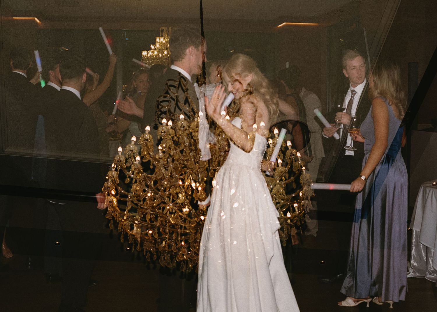 People dancing at an elegant reception with a stunning gold chandelier glowing in the background.