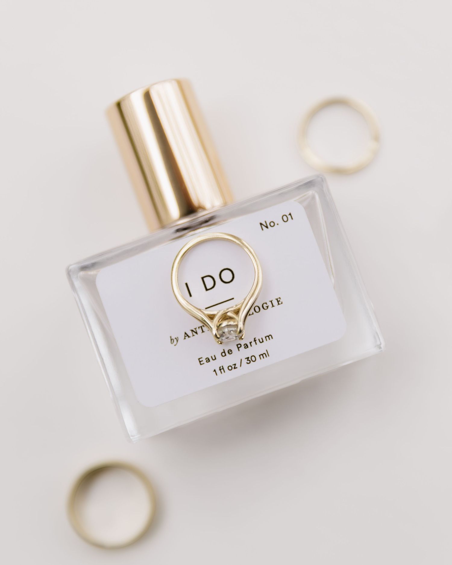Perfume bottle labeled 'I DO' with gold rings on light background.