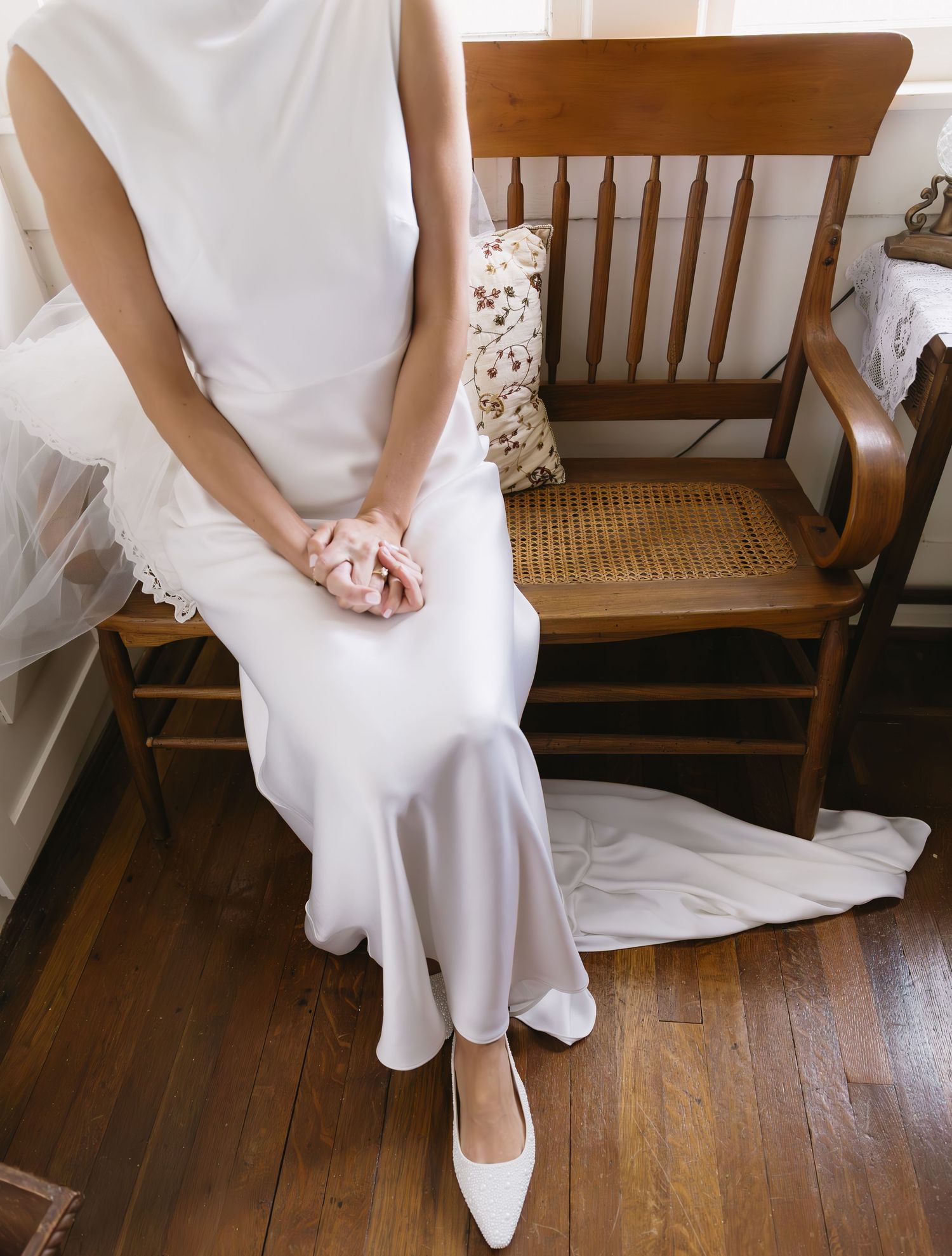 Detail shot of bride's white wedding dress and shoes against wooden floor and bench.