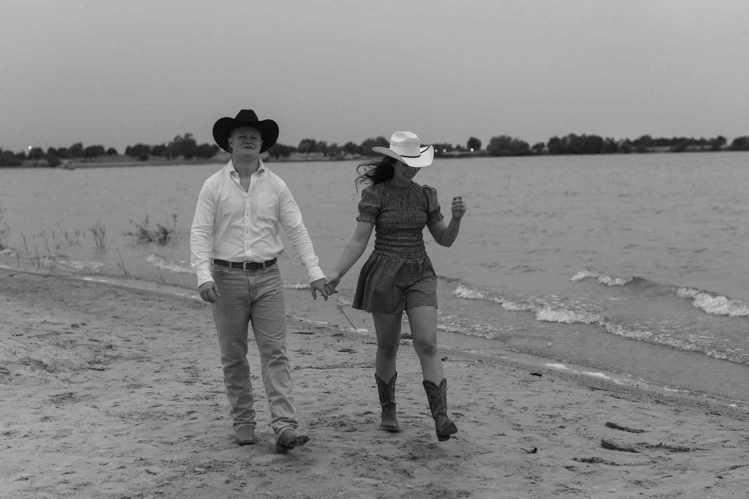 Couple walking hand in hand along a beach shoreline in black and white.