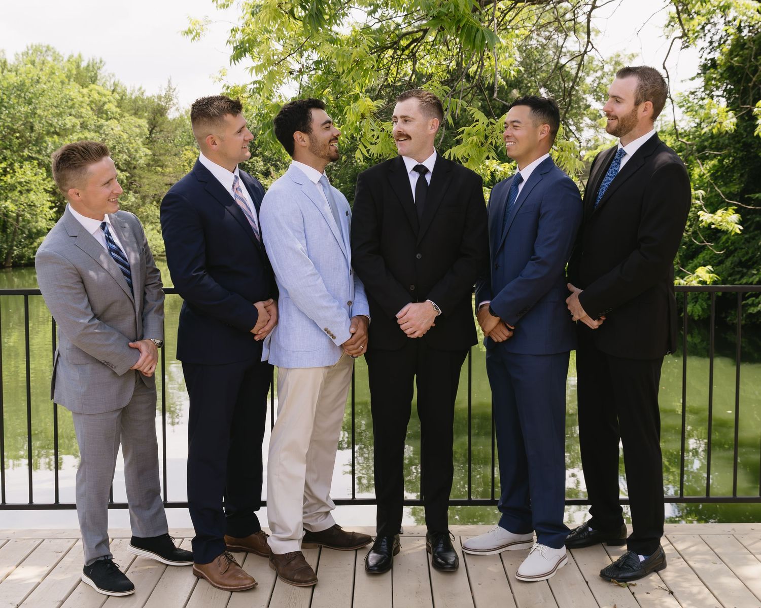 Wedding party members in suits pose together on outdoor terrace.