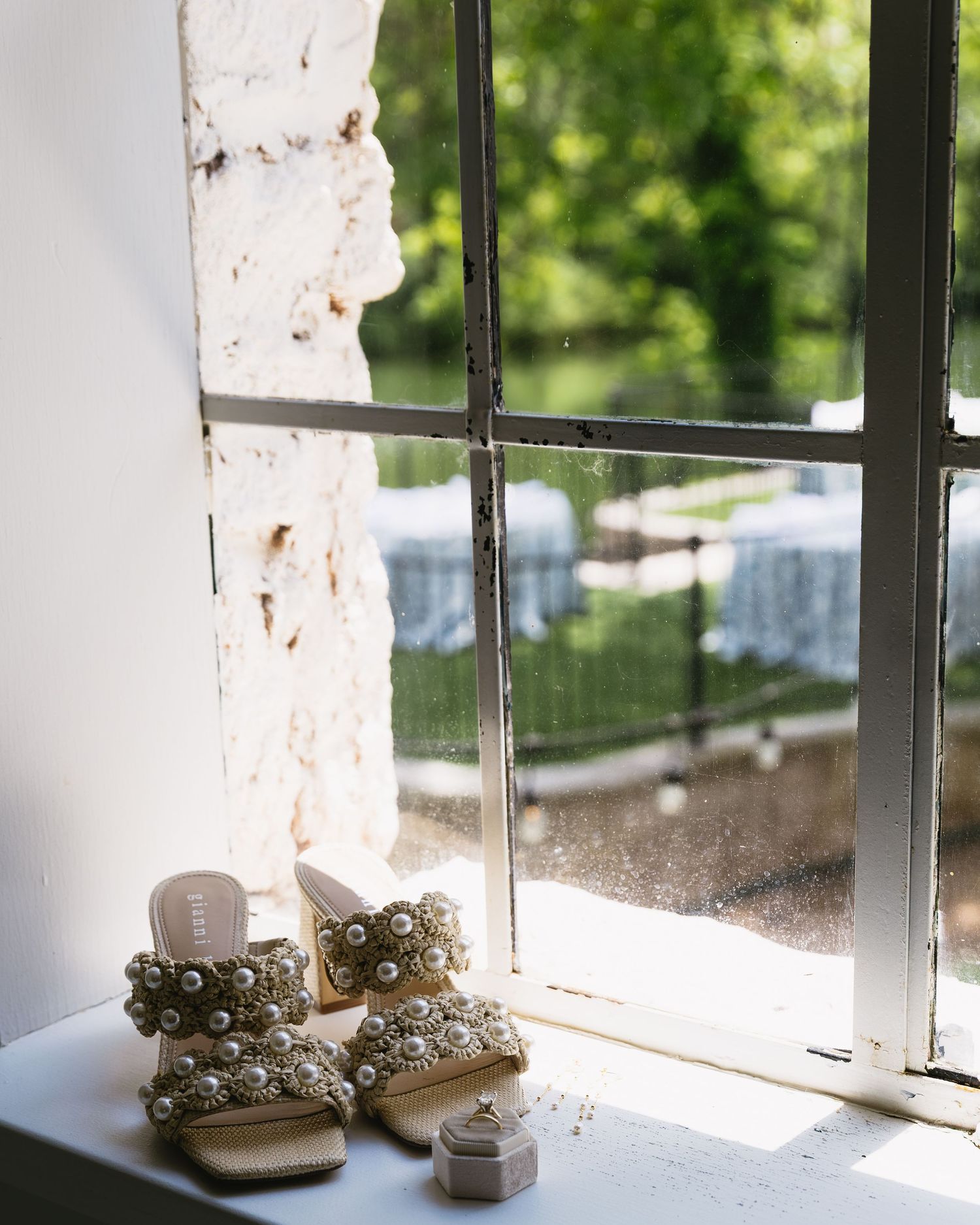 Pearl-embellished bridal shoes placed on a sunlit windowsill creating dramatic lighting.