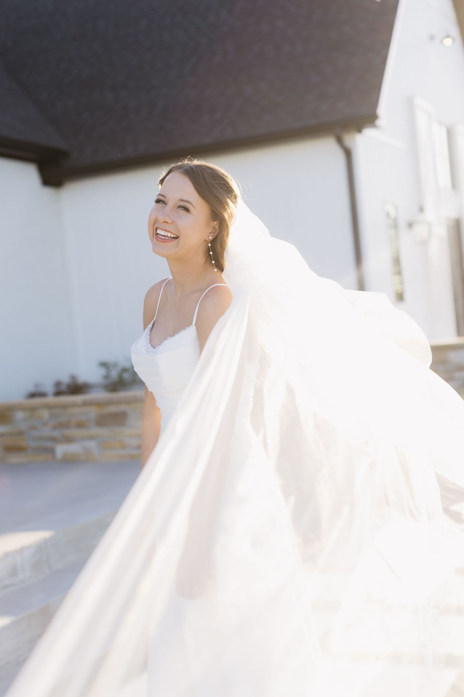 A flowing white wedding veil catches sunlight as it billows in the breeze against an architectural backdrop.
