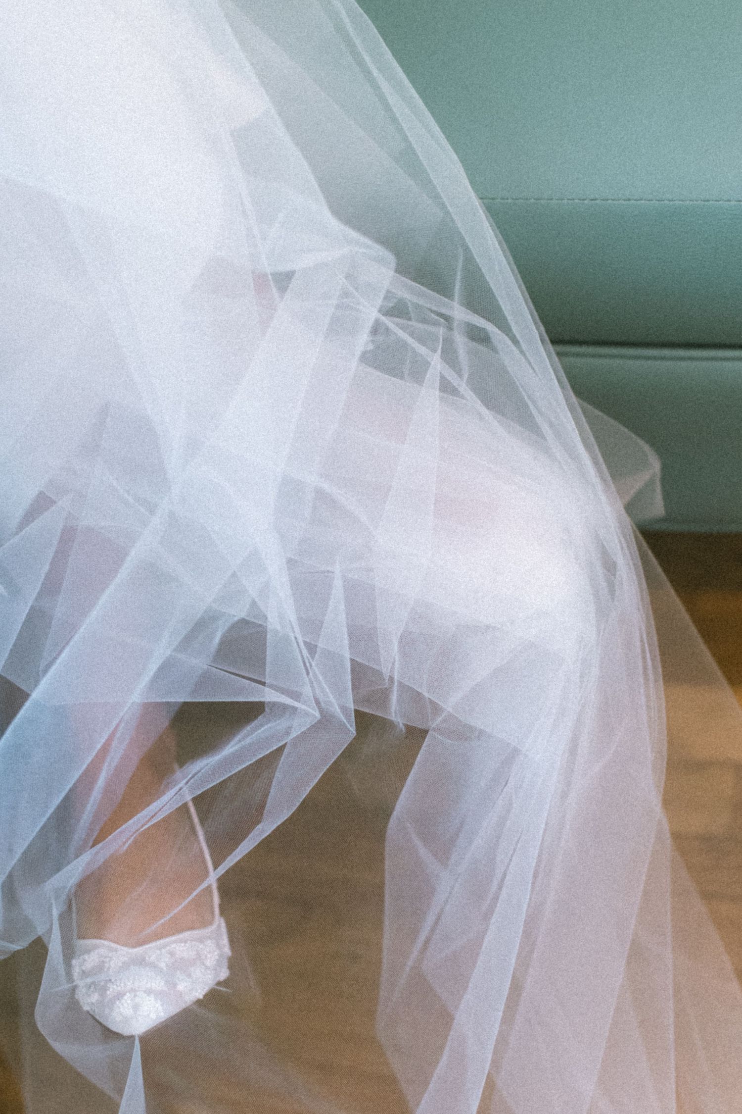 A flowing white tulle bridal veil cascades elegantly against a soft blue-green wall.