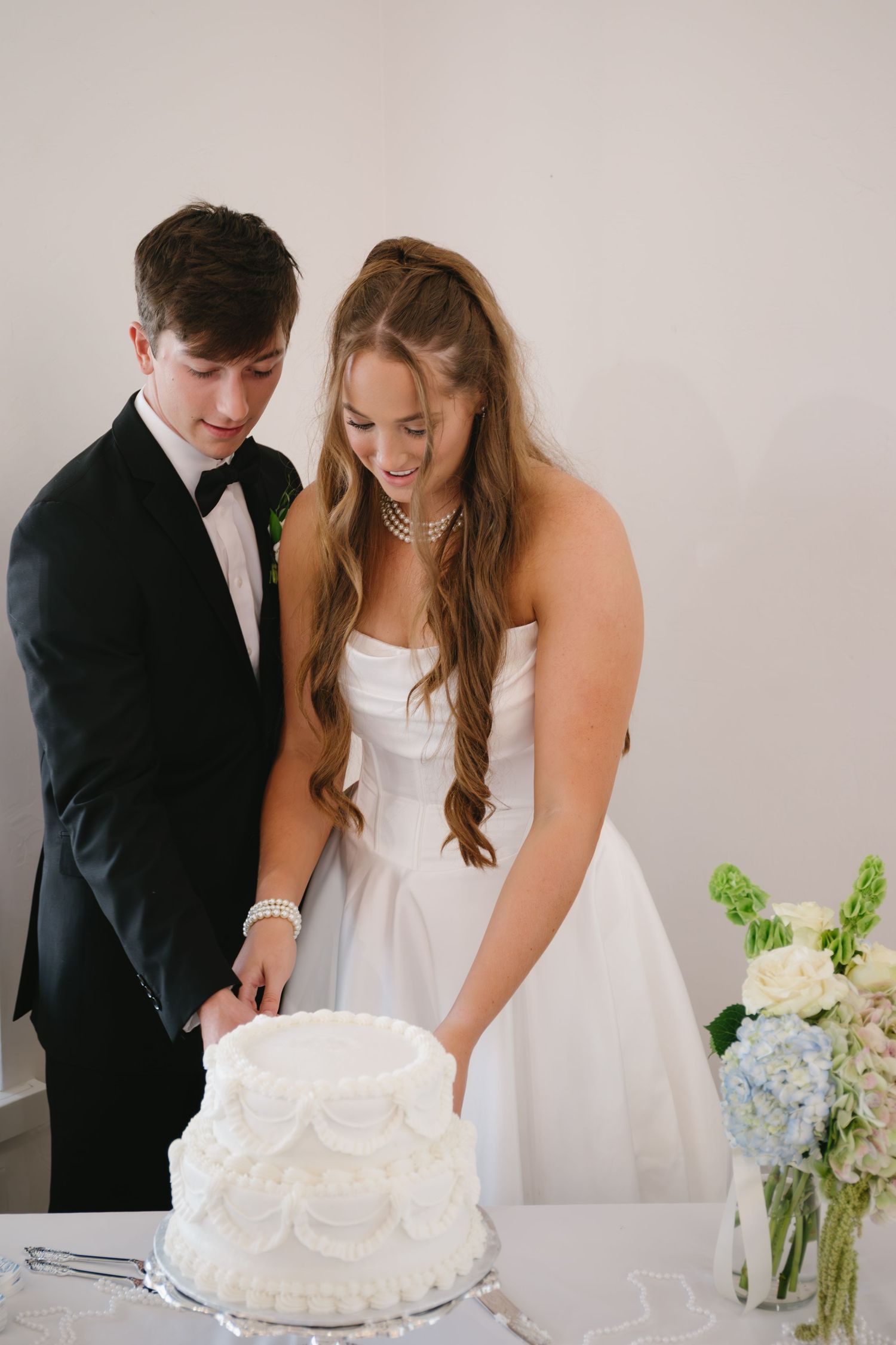Couple in wedding attire cutting their white tiered wedding cake together.