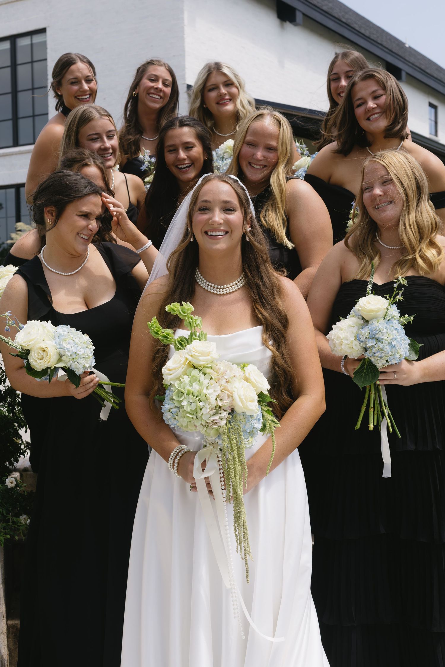 Wedding party photo with bridesmaids in black dresses holding floral bouquets.