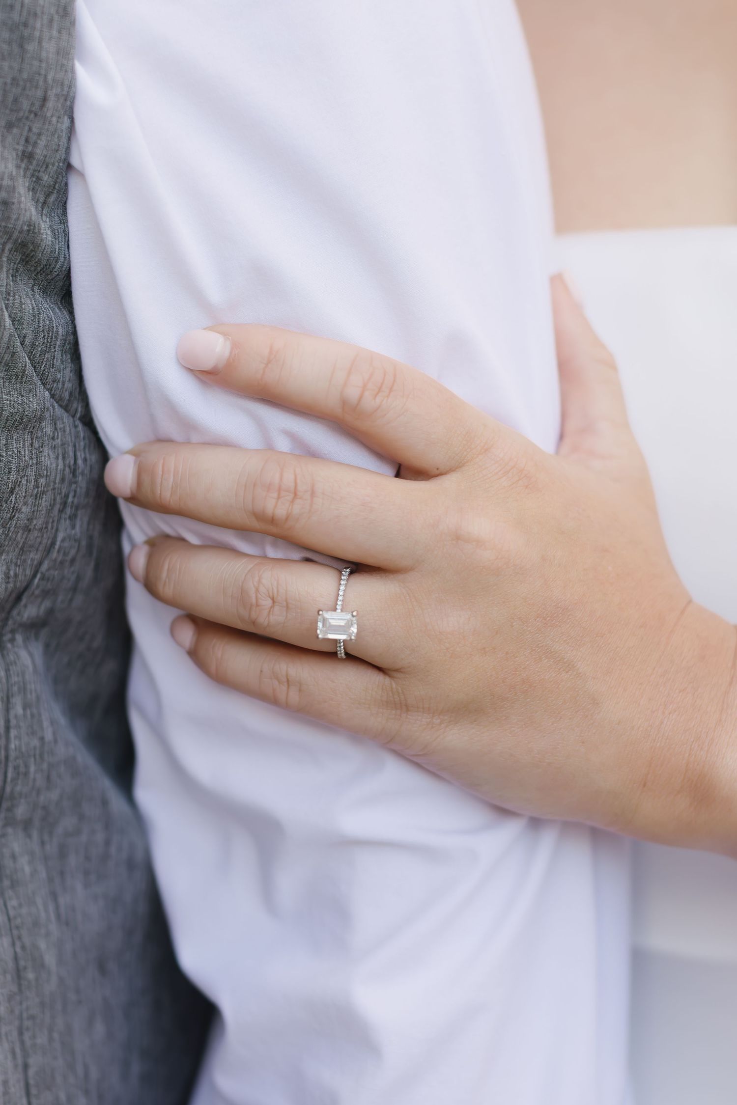 Close-up shots of a hand wearing an elegant emerald-cut diamond solitaire engagement ring against white fabric.