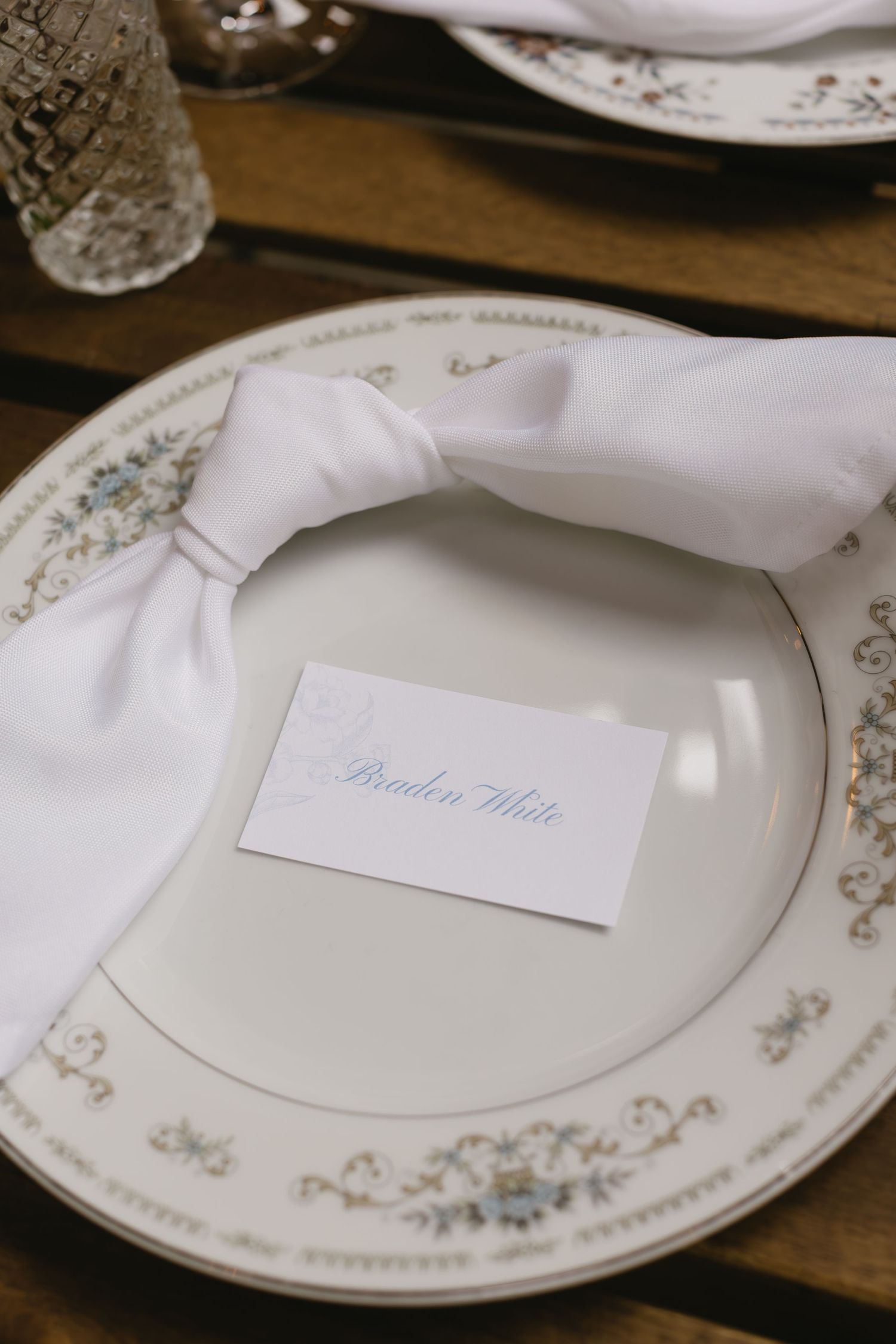 Elegant place setting with white napkin and name card on decorative china plate.