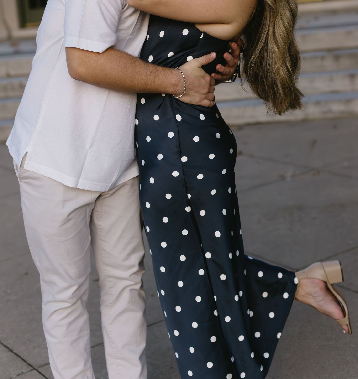 Sweet candid moment between couple in polka dots and white against architectural backdrop.