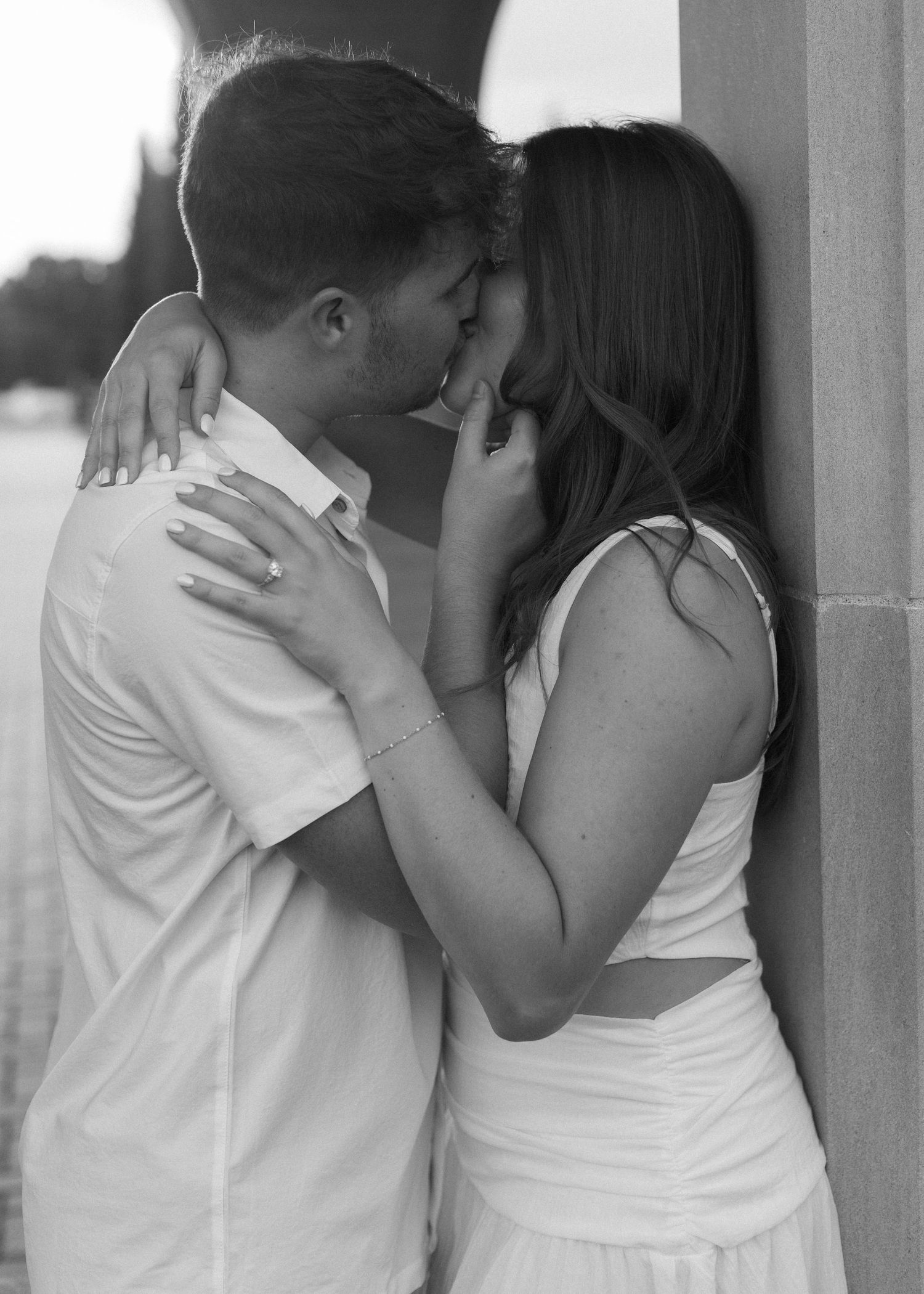 A romantic black and white photo of a couple sharing an intimate kiss against a wall.