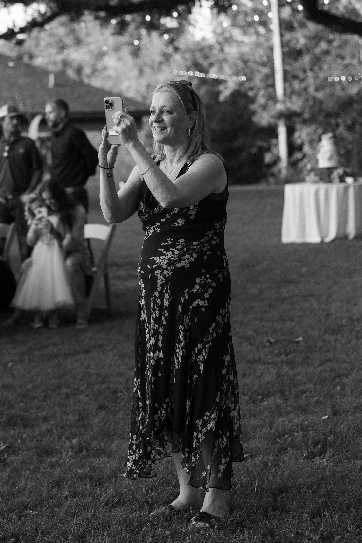 Guest in black lace dress dances at outdoor wedding reception.
