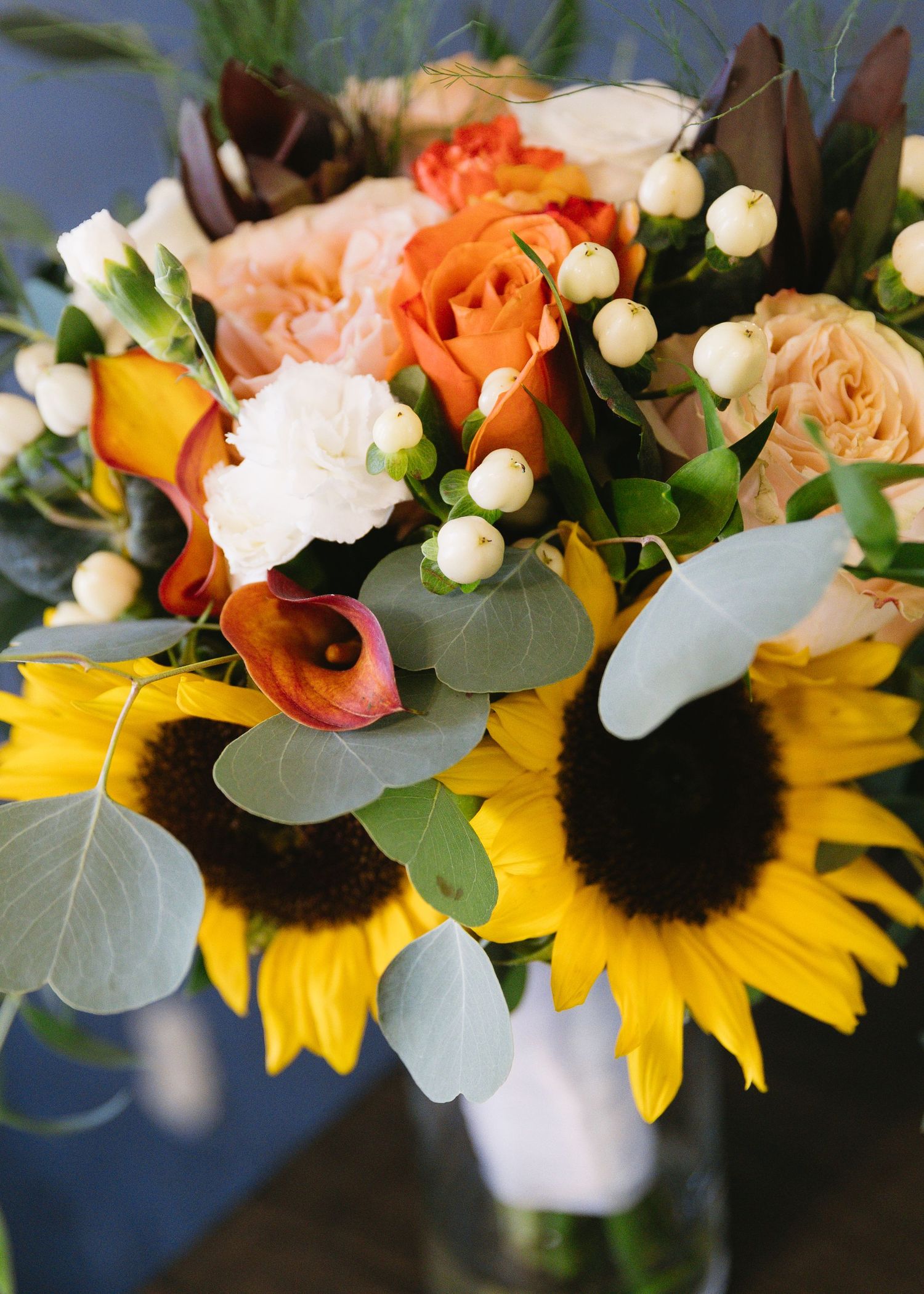 Stunning floral arrangement with sunflowers, white roses, and eucalyptus in rustic setting.