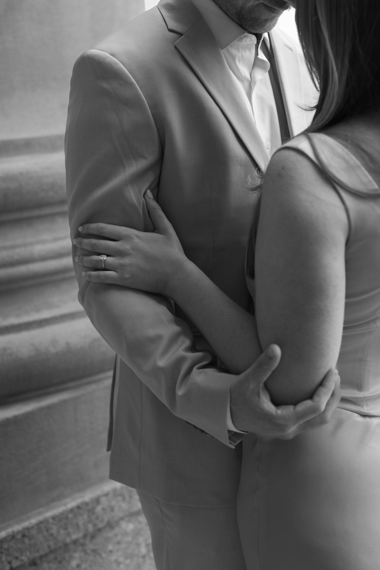 Black and white close-up of couple embracing, showing details of formal attire.