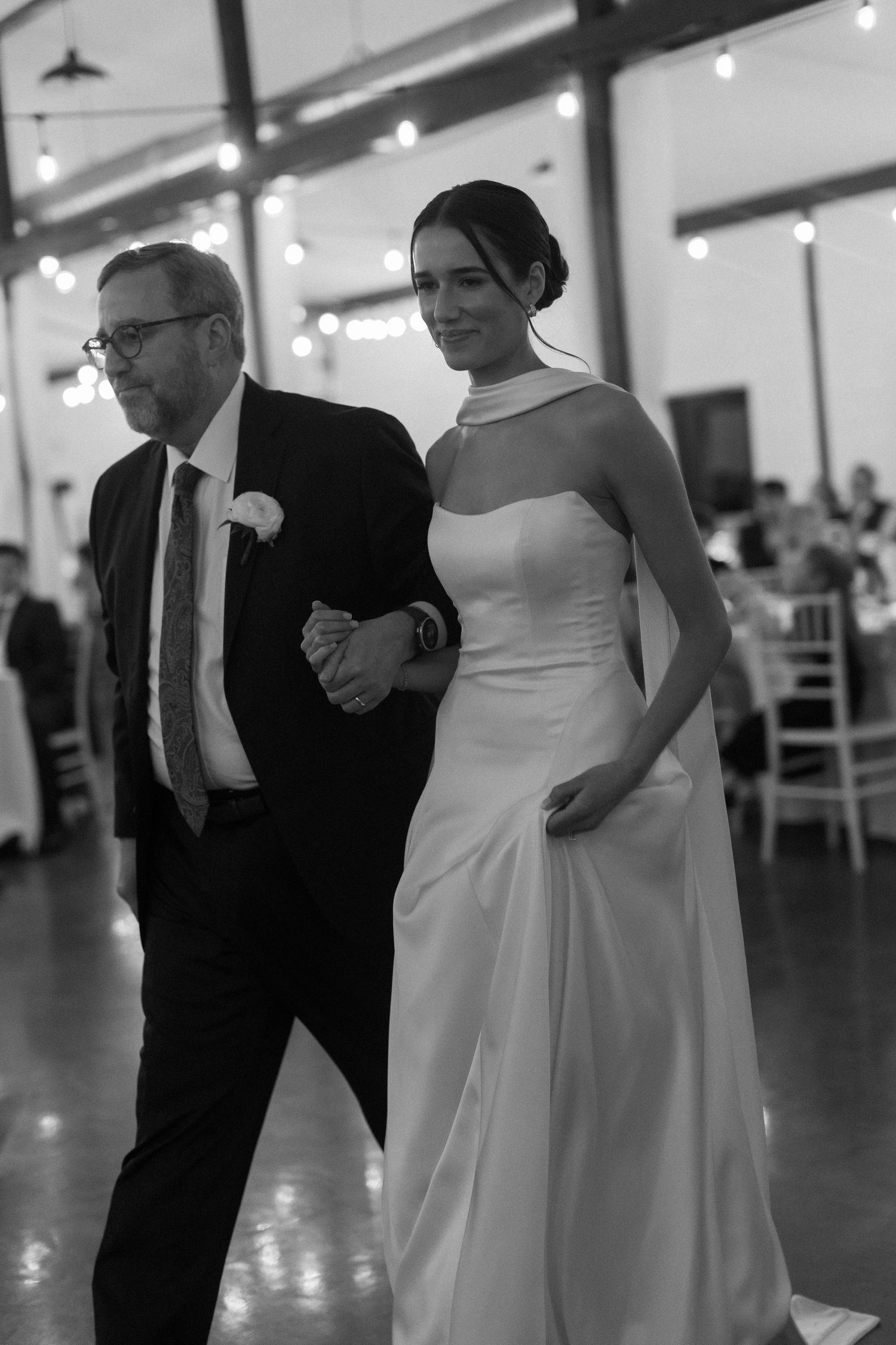 Couple sharing their first dance in an elegant reception hall with string lights overhead.