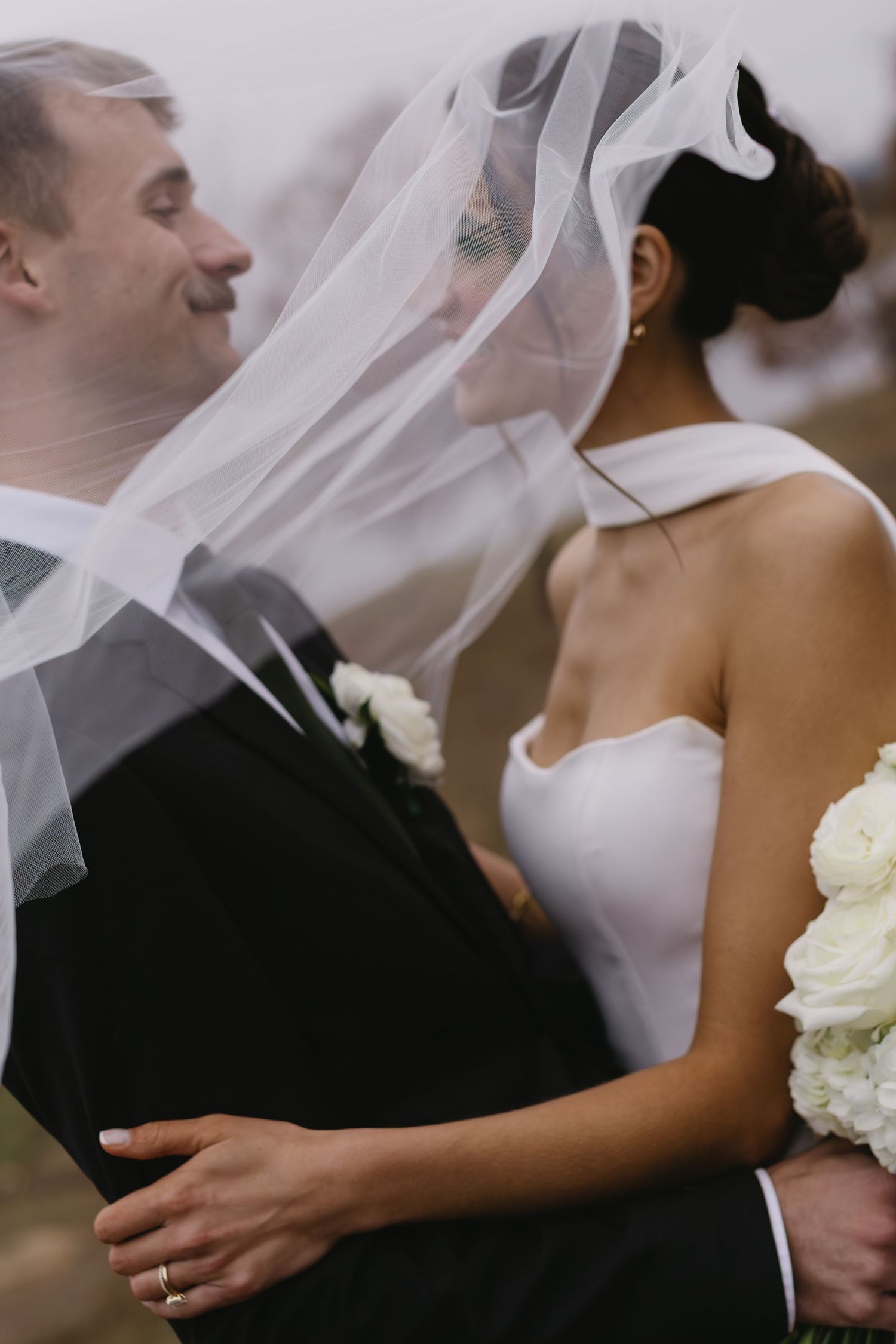 Close-up of newlyweds sharing a tender moment with flowing veil and white bouquet.