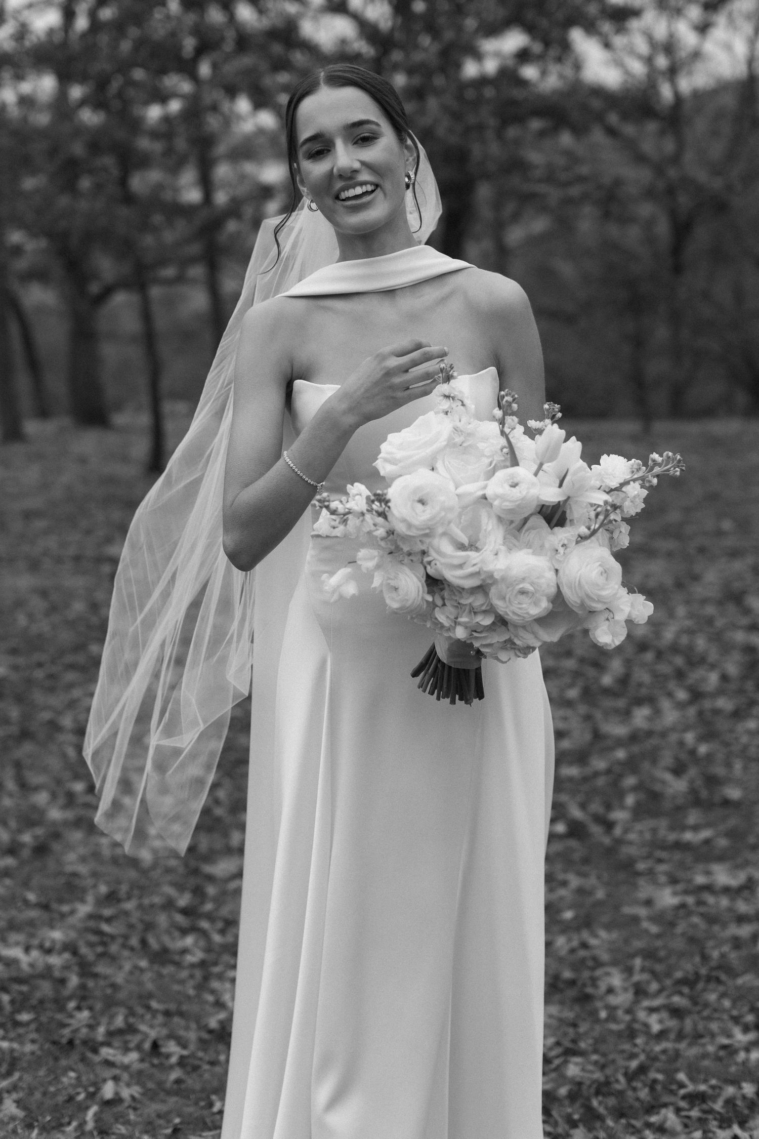 Black and white portrait of a bride holding a white bouquet in an outdoor setting.