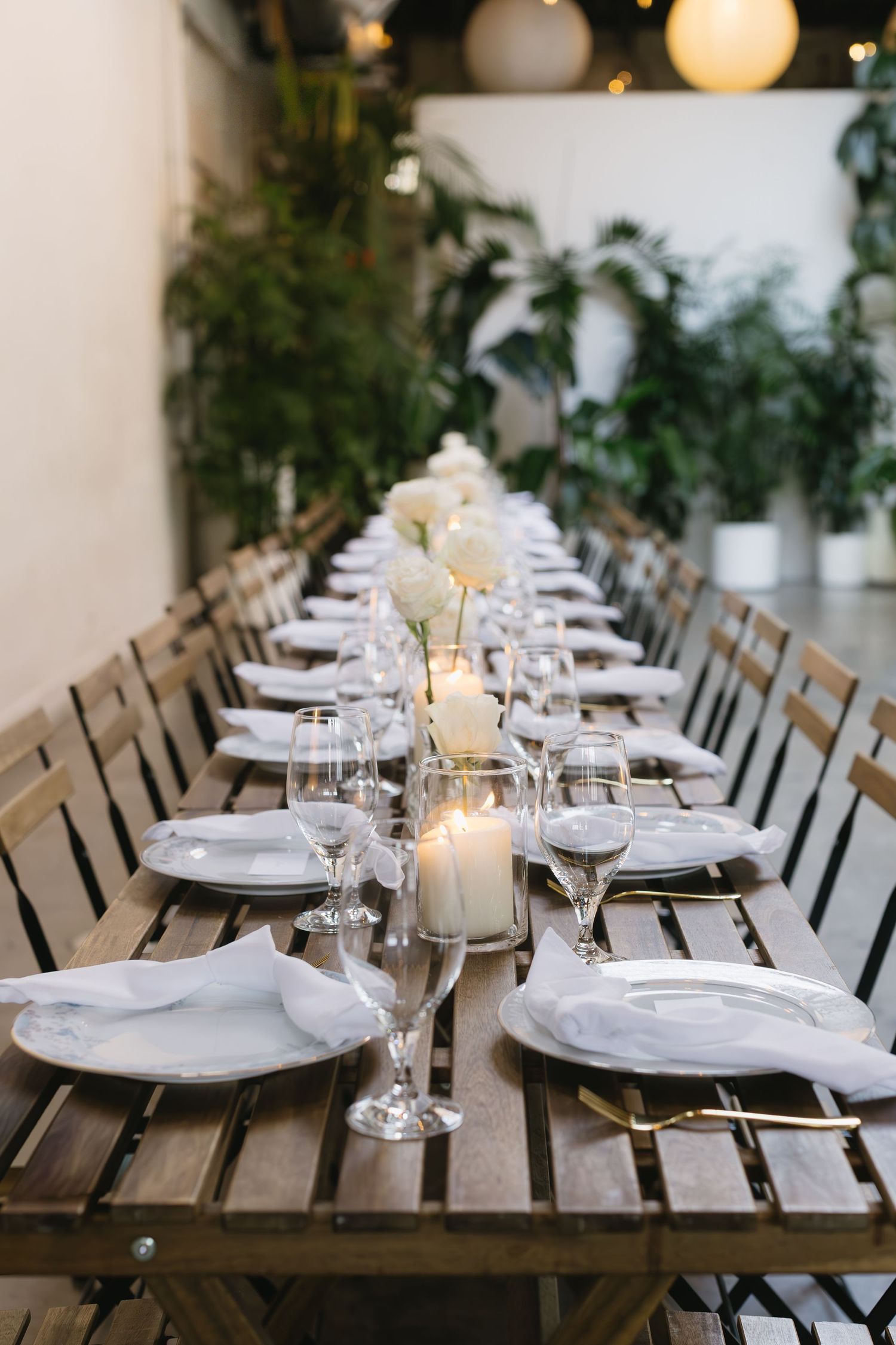 An elegant table setting with white plates and glowing candles under string lights creates a romantic atmosphere.