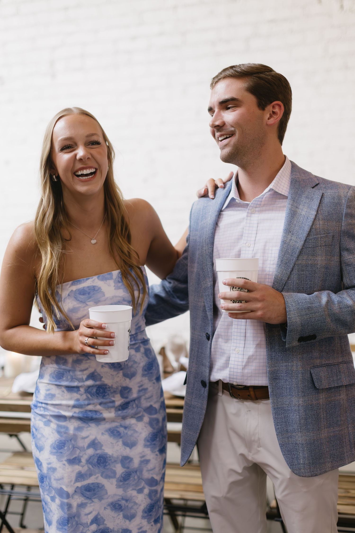 A couple laughs together while holding drinks at an elegant event.