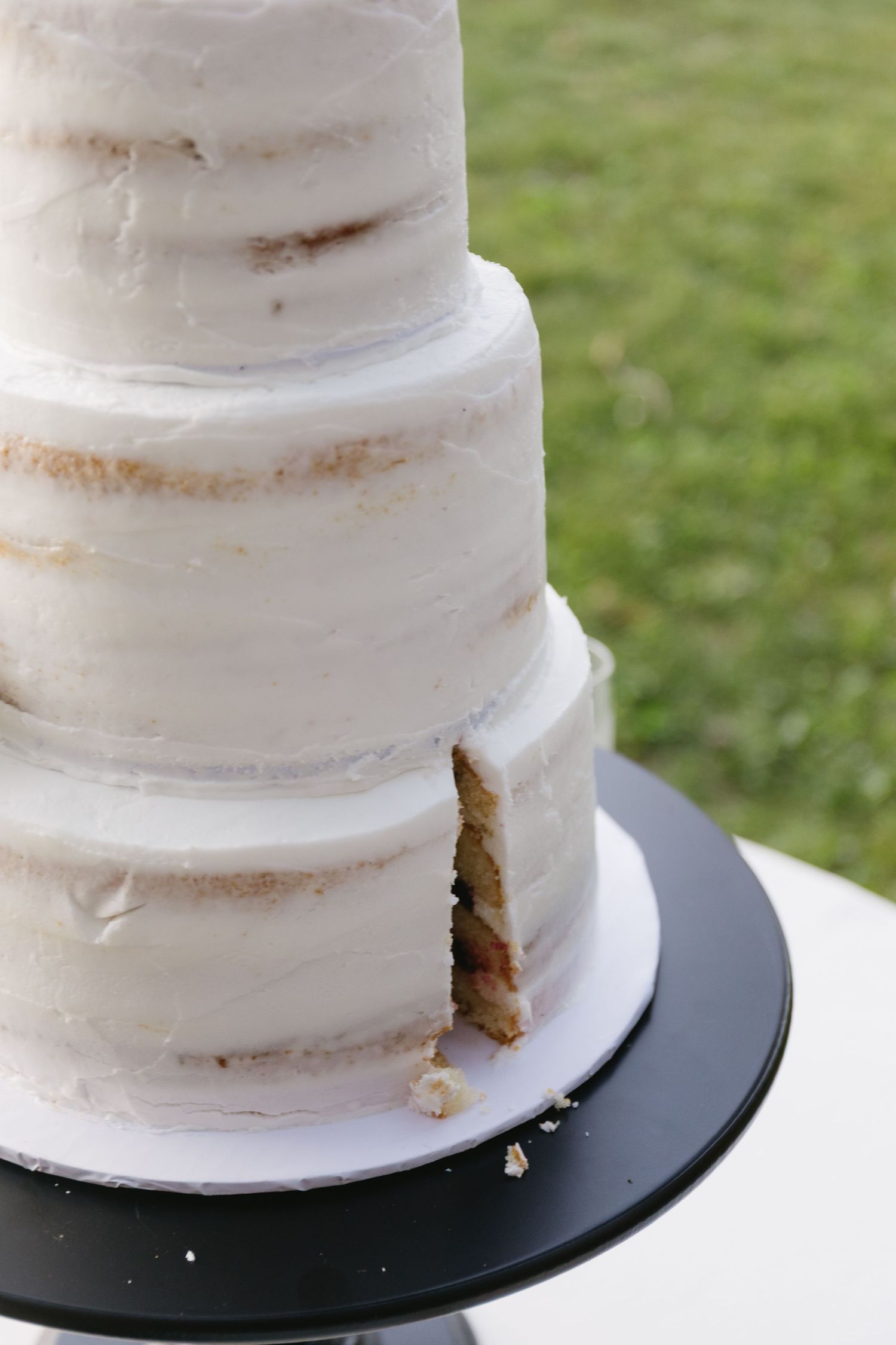 Detail shot of a semi-naked white wedding cake on a black stand showing textured frosting layers.