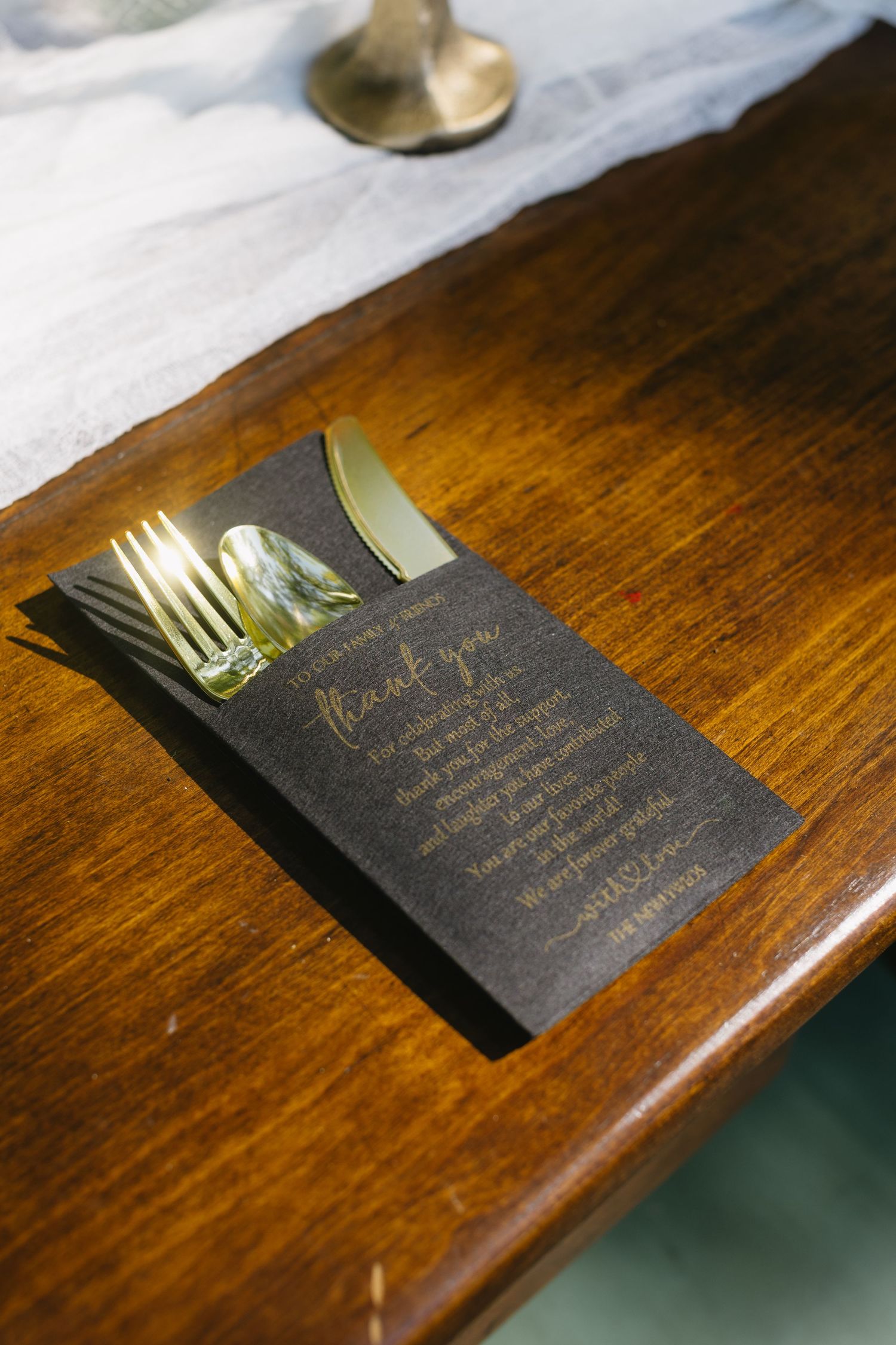 Elegant black and gold wedding menu cards with gold cutlery on dark wooden table.