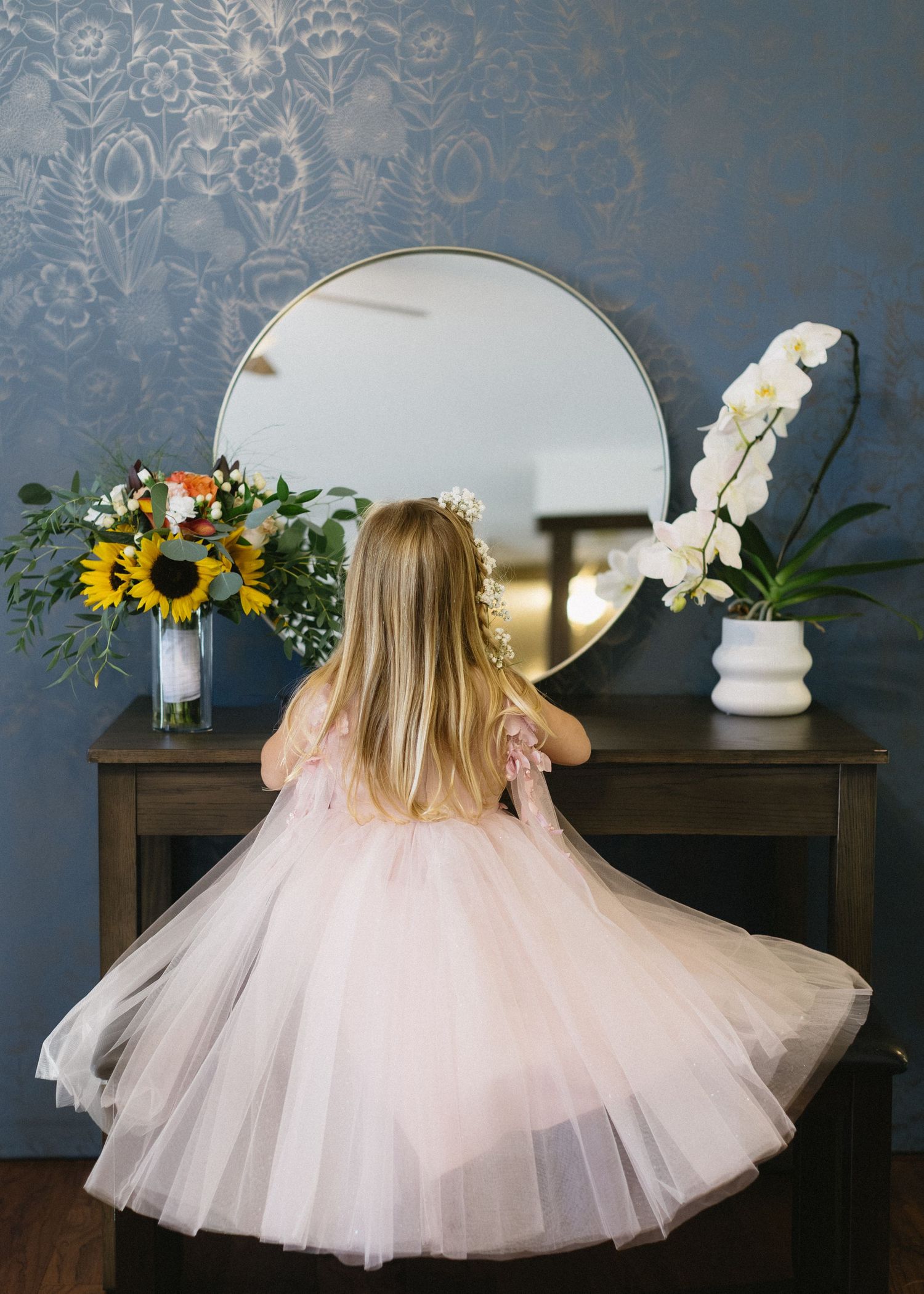 Ethereal tulle skirt of a blush pink wedding dress shown in a twirling motion against a blue wall.