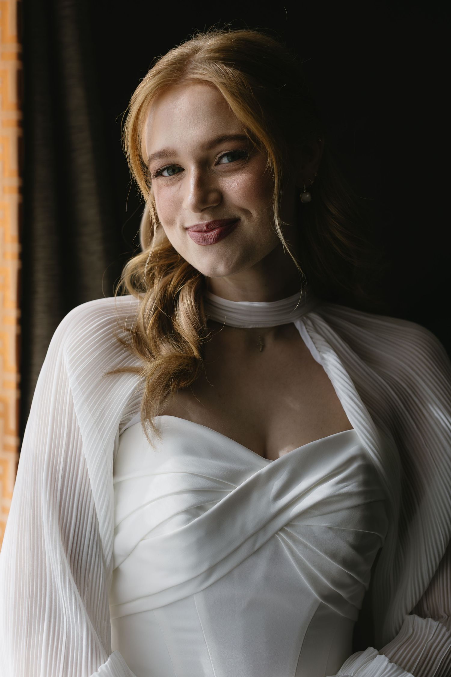 Close-up portrait shots of a bride in a white dress with pleated sleeves against a dark background.