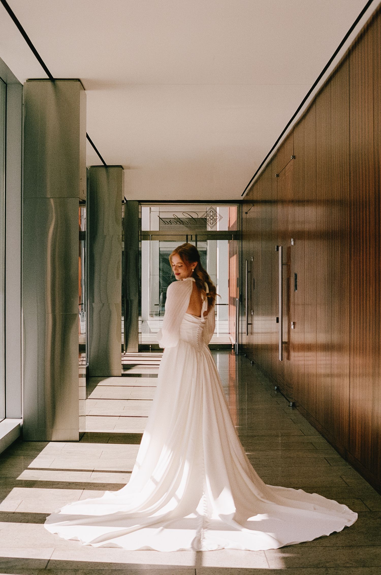 Sequence of bride in flowing white wedding gown with long train in modern hallway.