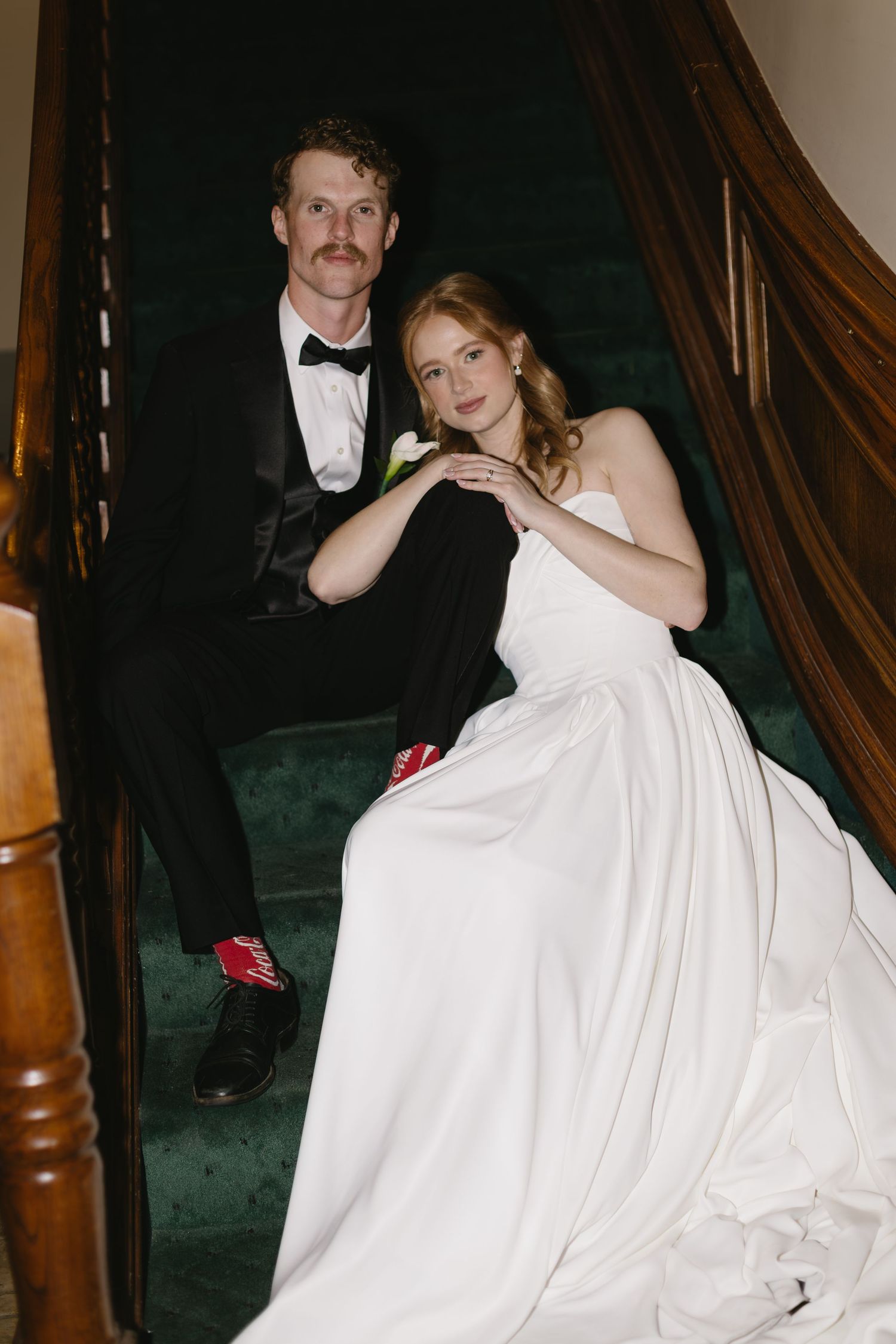 A couple descends elegant wooden stairs during their wedding celebration.