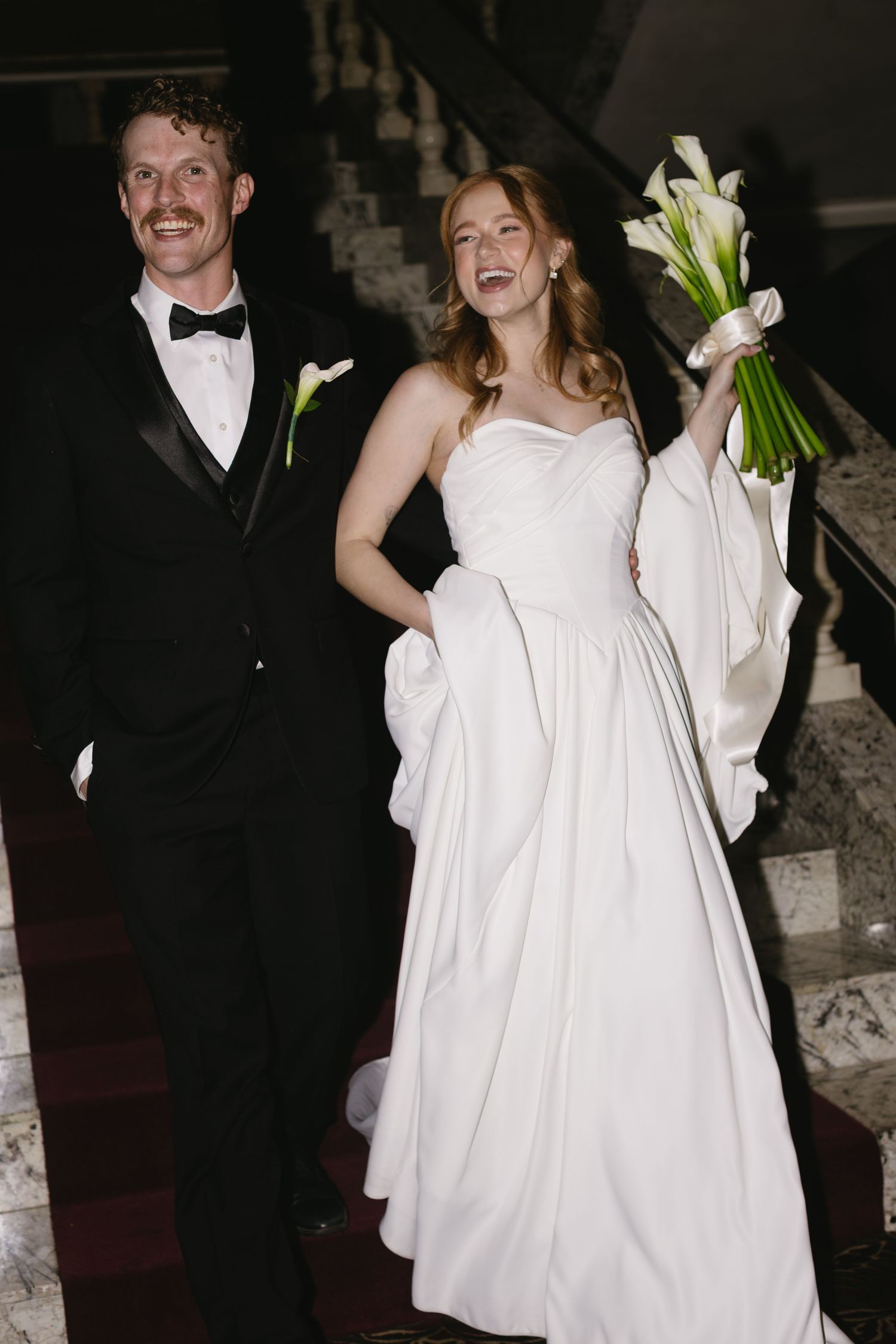 A bride in a flowing white dress holds a bouquet of calla lilies while dancing with her groom.