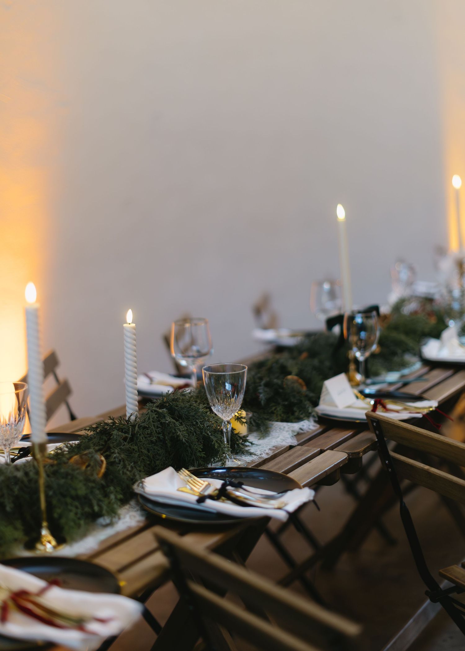 Romantic wedding table setting with candles, greenery, and place settings on rustic wooden tables.