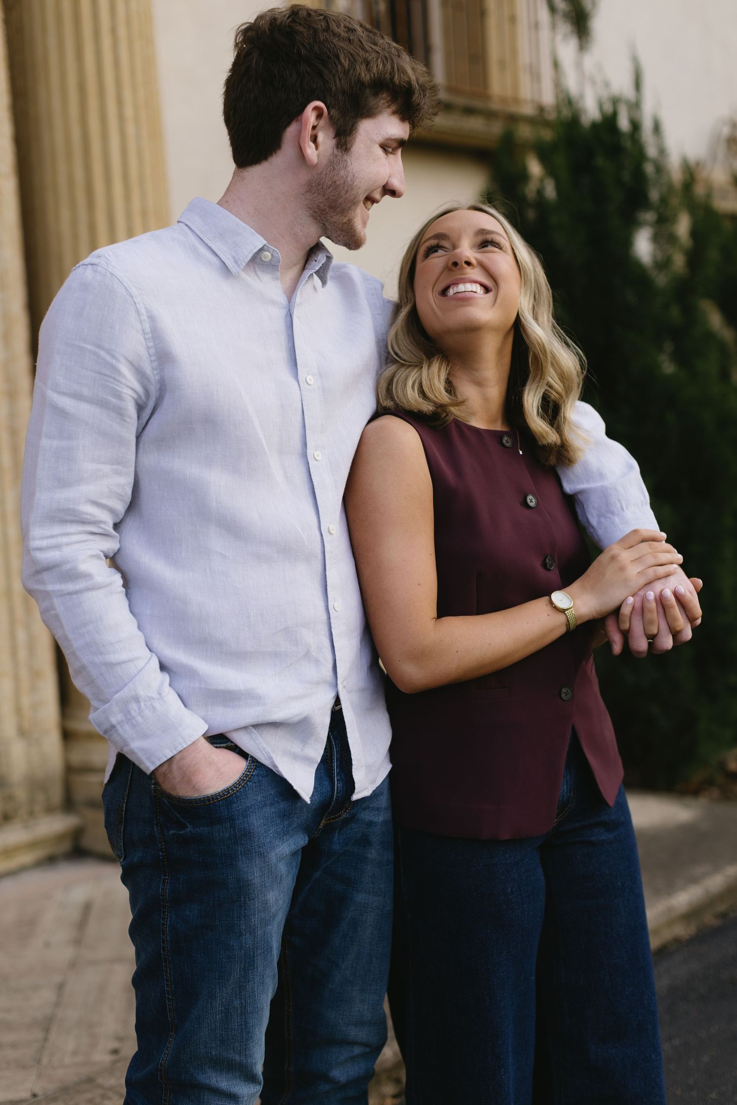A couple shares a joyful moment together while posing against a classical architectural backdrop.