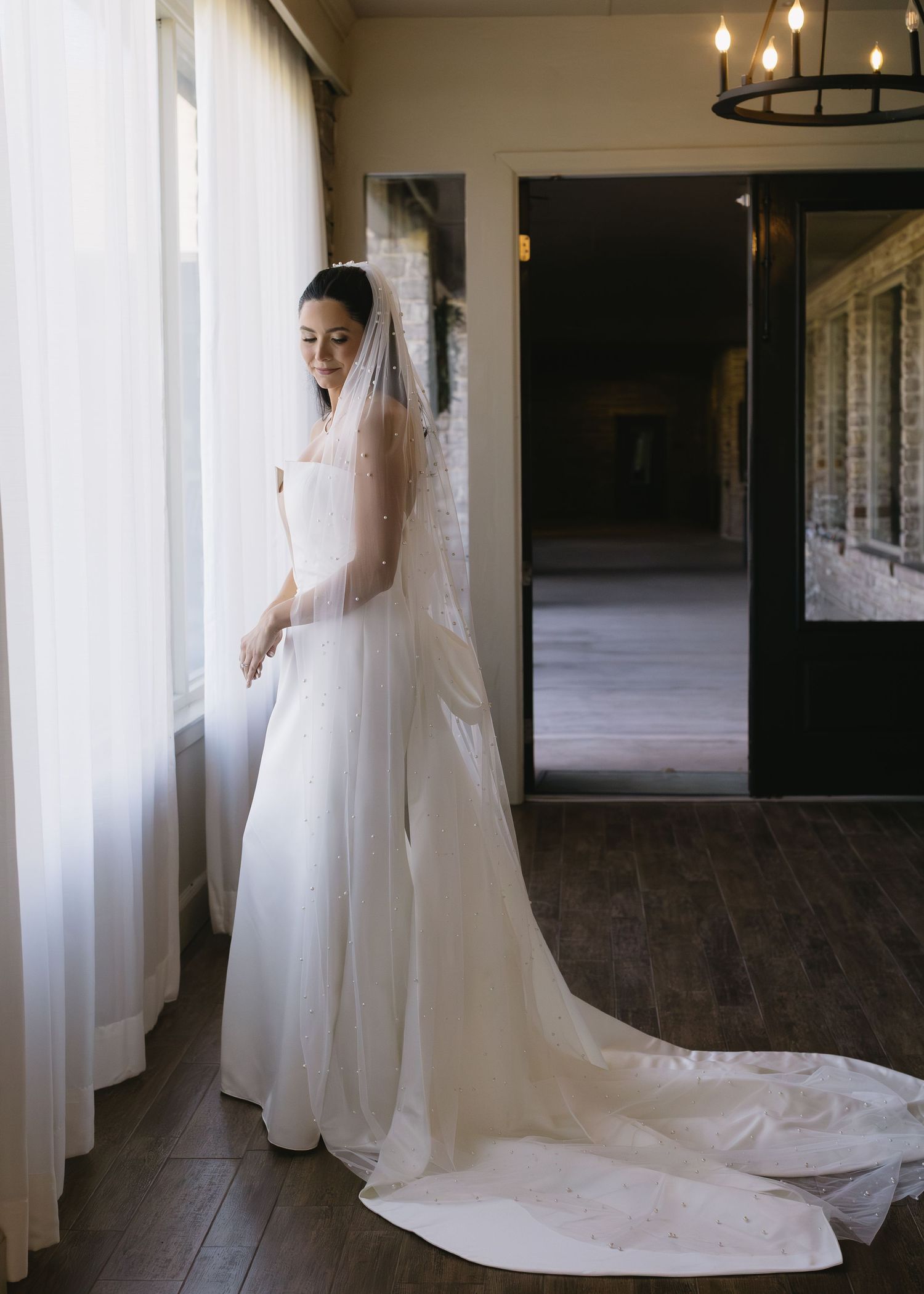Wide shot of a bride in a white gown with long train standing between elegant white columns.