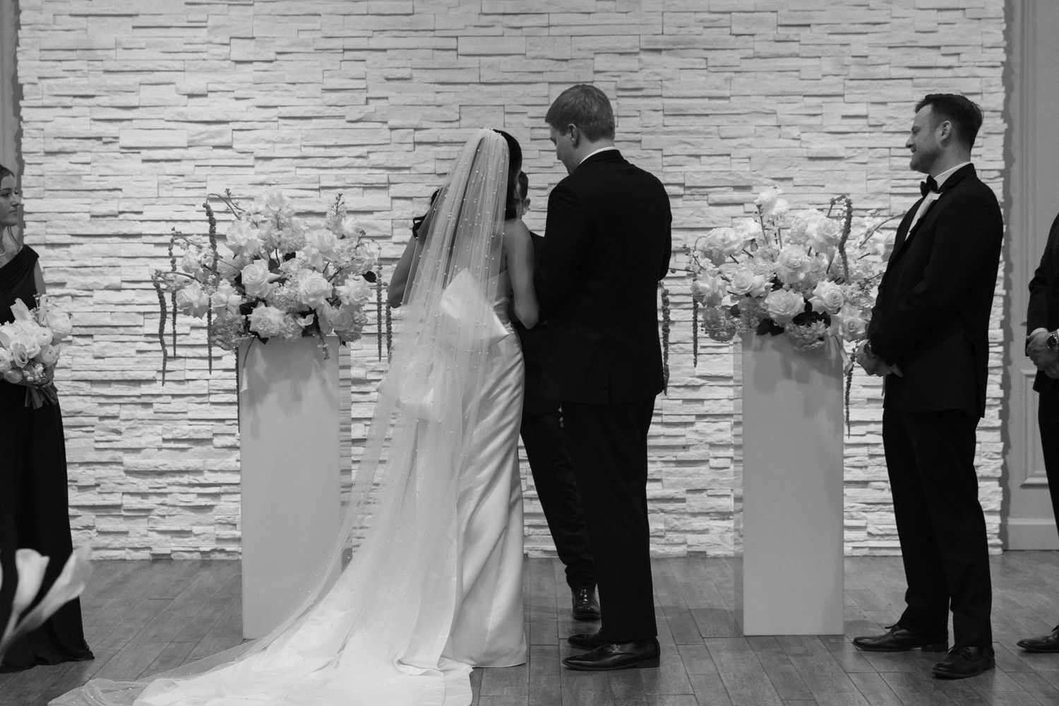 Black and white wedding ceremony photos showing couple exchanging vows with white floral decor.