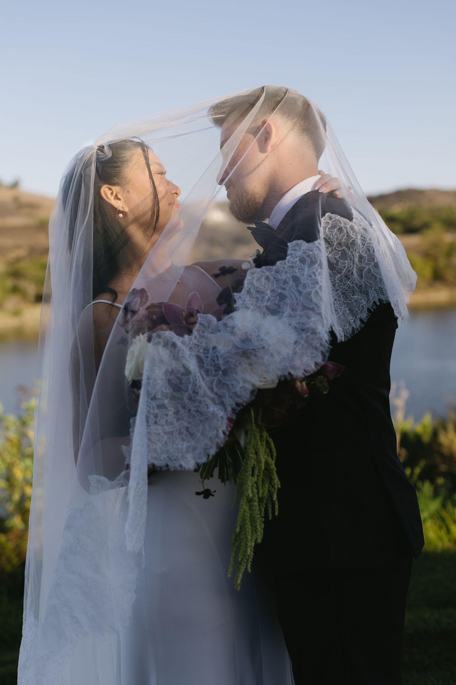 Wedding couple embraces during sunset photoshoot with lake and natural scenery in background.