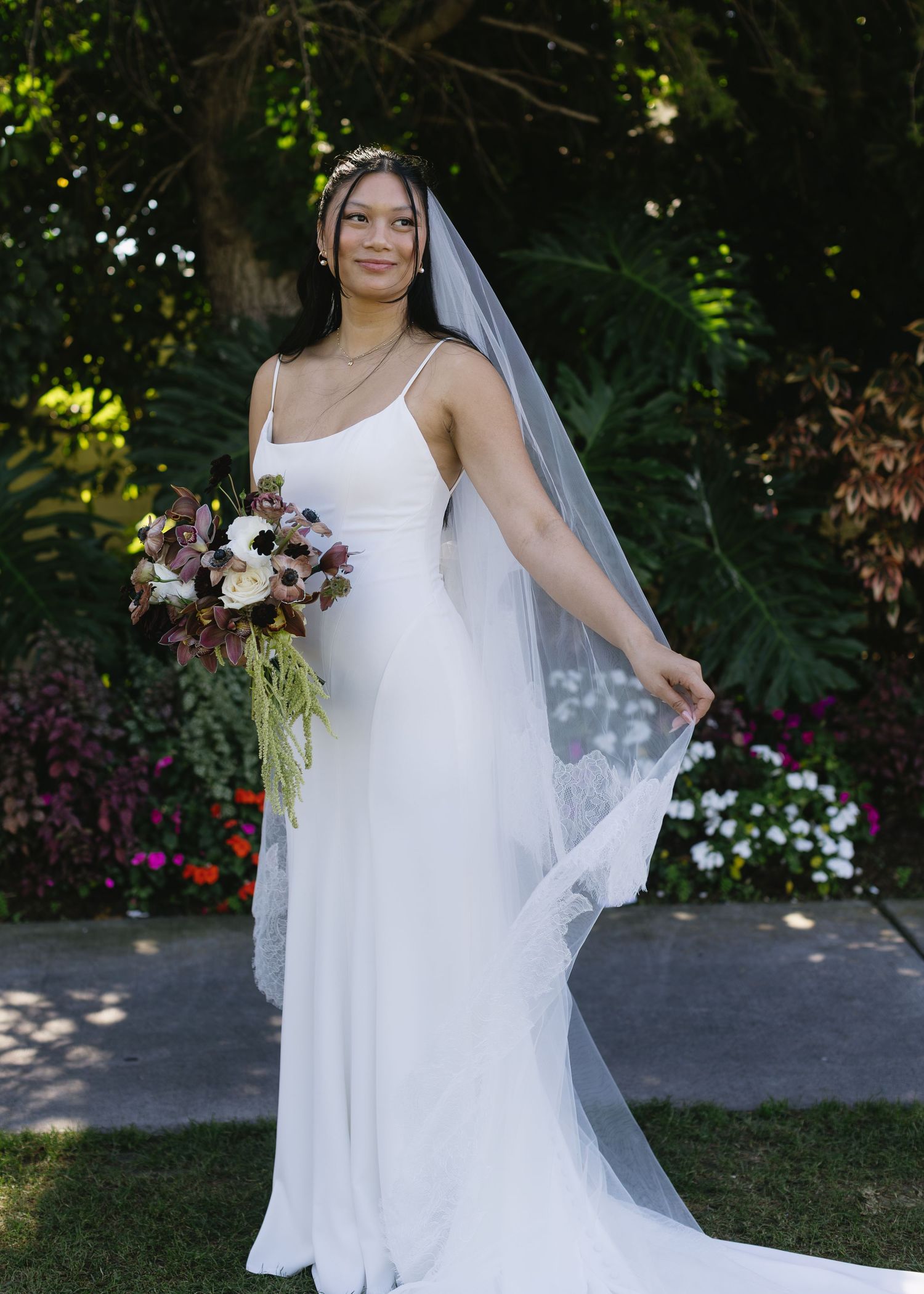 Elegant bride in simple white wedding dress and veil posing in a garden setting.