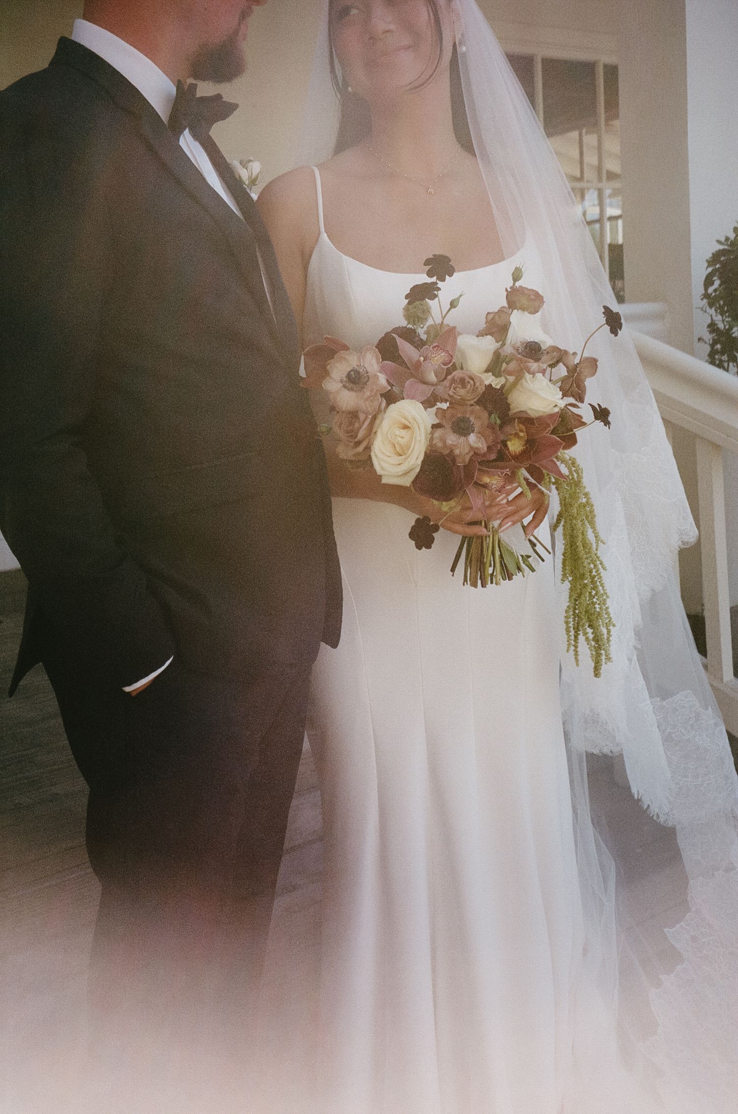 Close-up of bride in white dress holding romantic burgundy and blush bouquet.