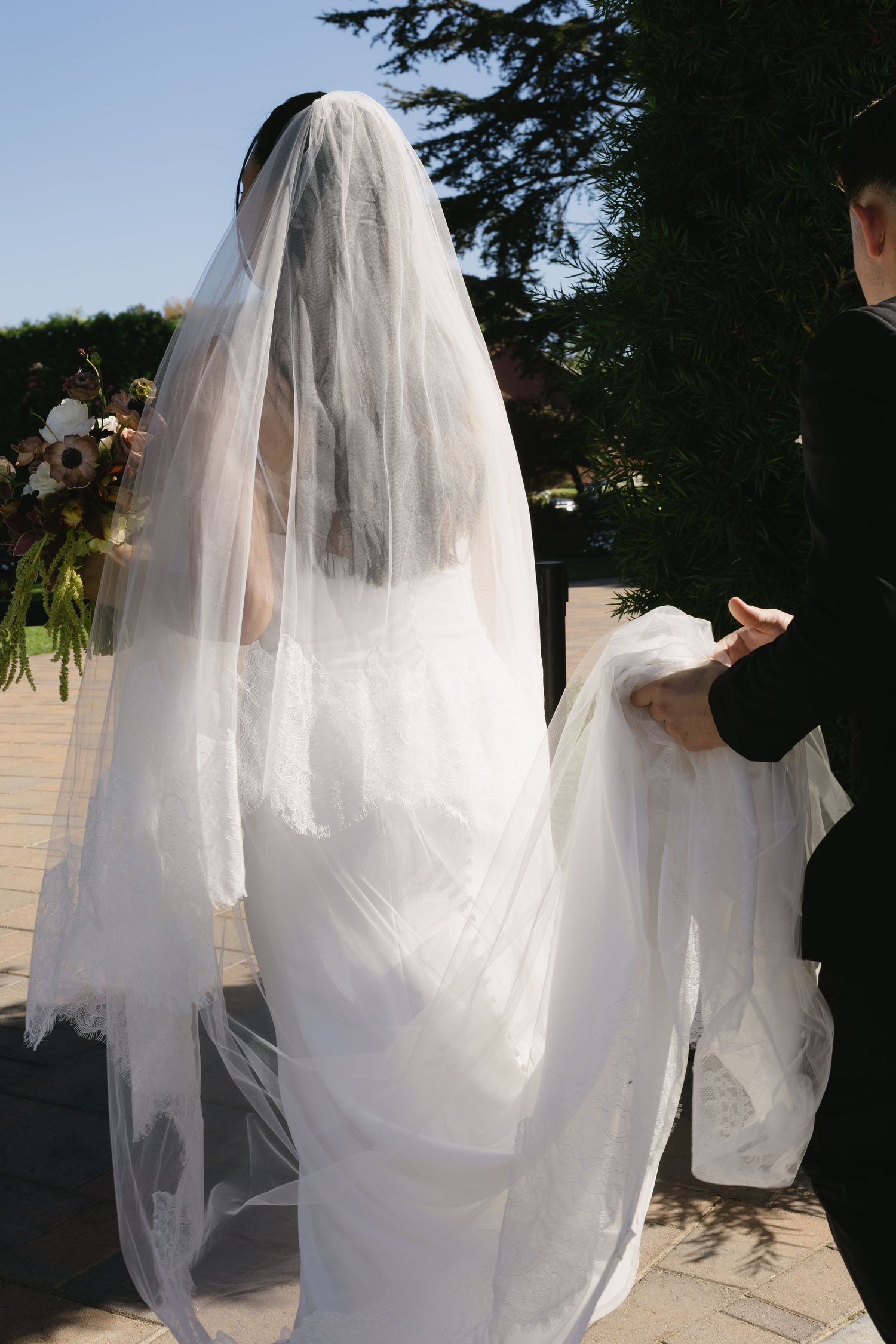 A flowing white wedding veil and dress captured in an outdoor garden setting.