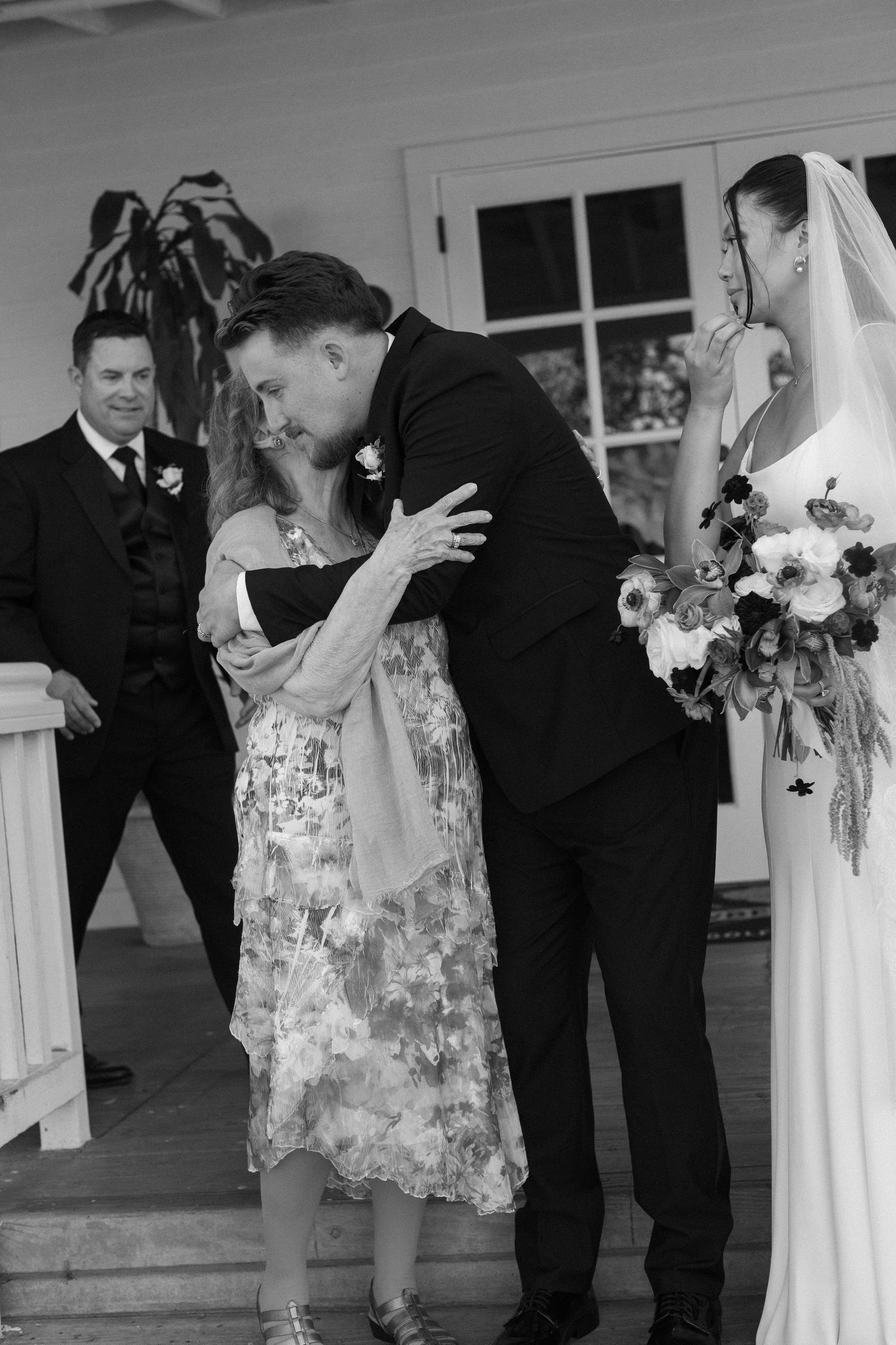 Wedding party members share emotional embraces during black and white photo session.