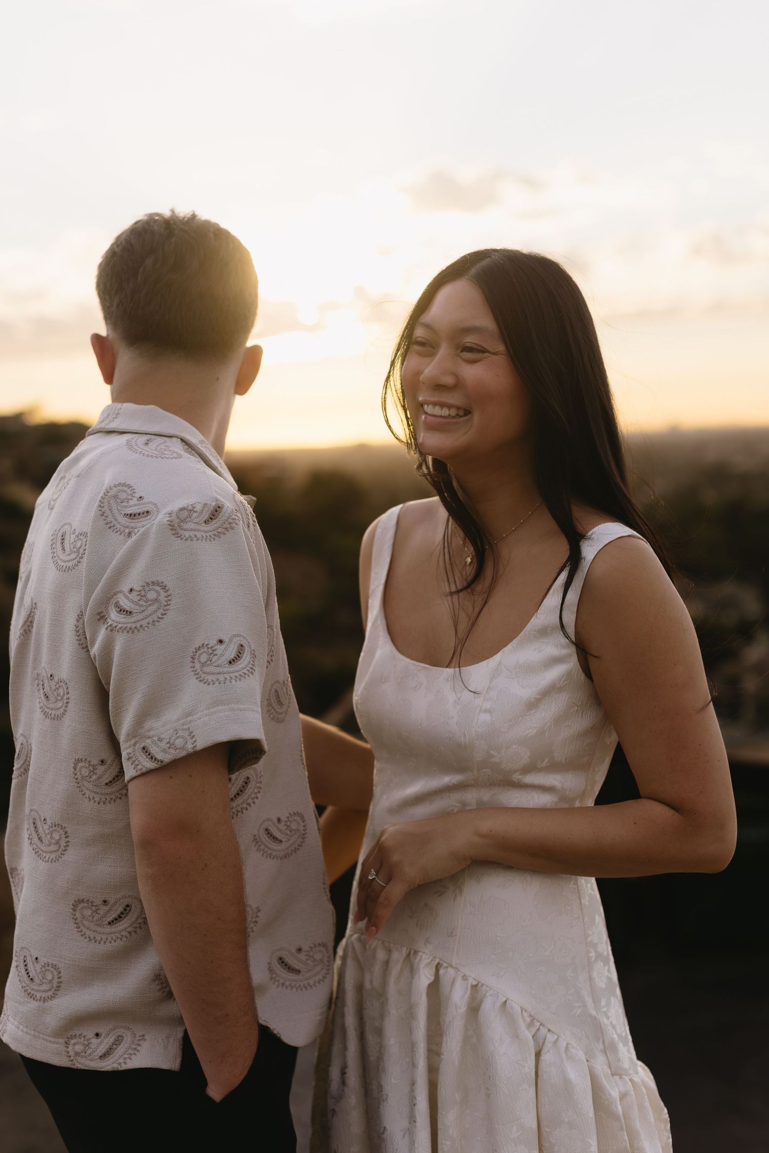 Couple embracing during sunset photoshoot, wearing matching white outfits.