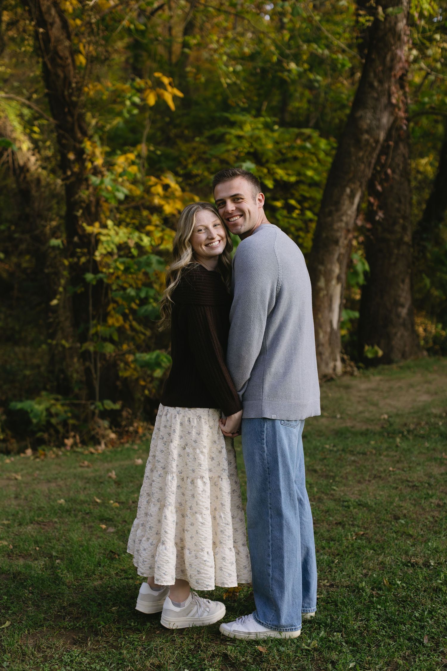 Romantic couple embracing outdoors in autumn park setting with golden foliage.