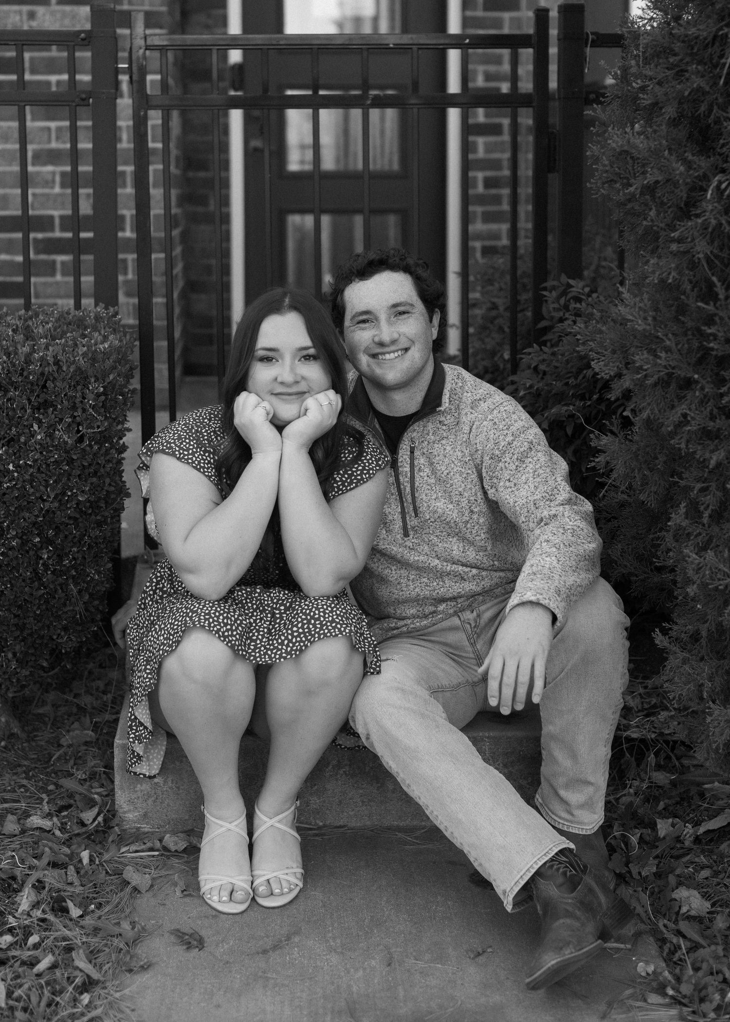 A couple sits casually together on brick steps during a playful photoshoot.