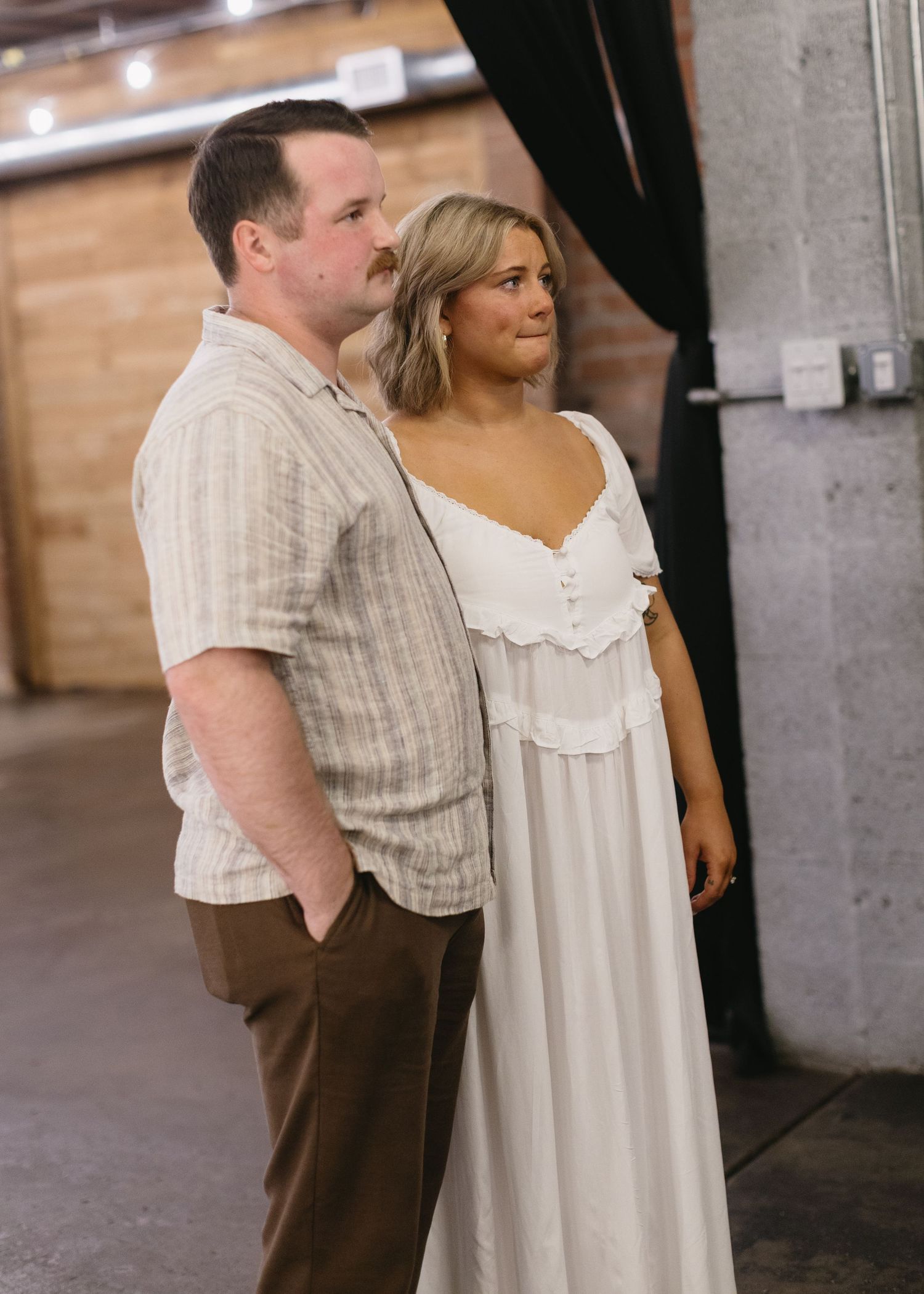 Couple in casual attire standing together in an industrial-style venue.