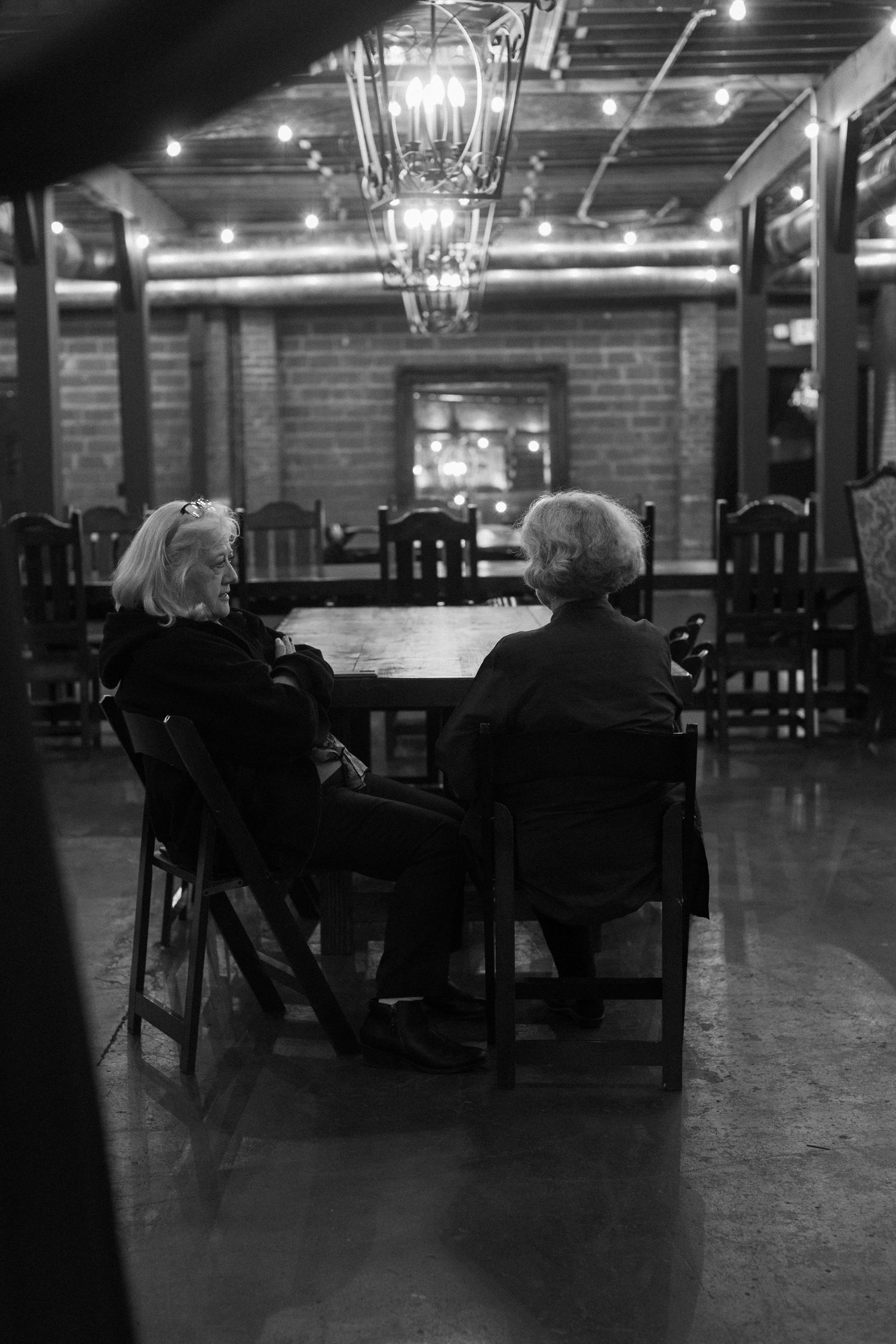 Dark reception venue with chandeliers and wooden chairs creating a moody atmosphere.