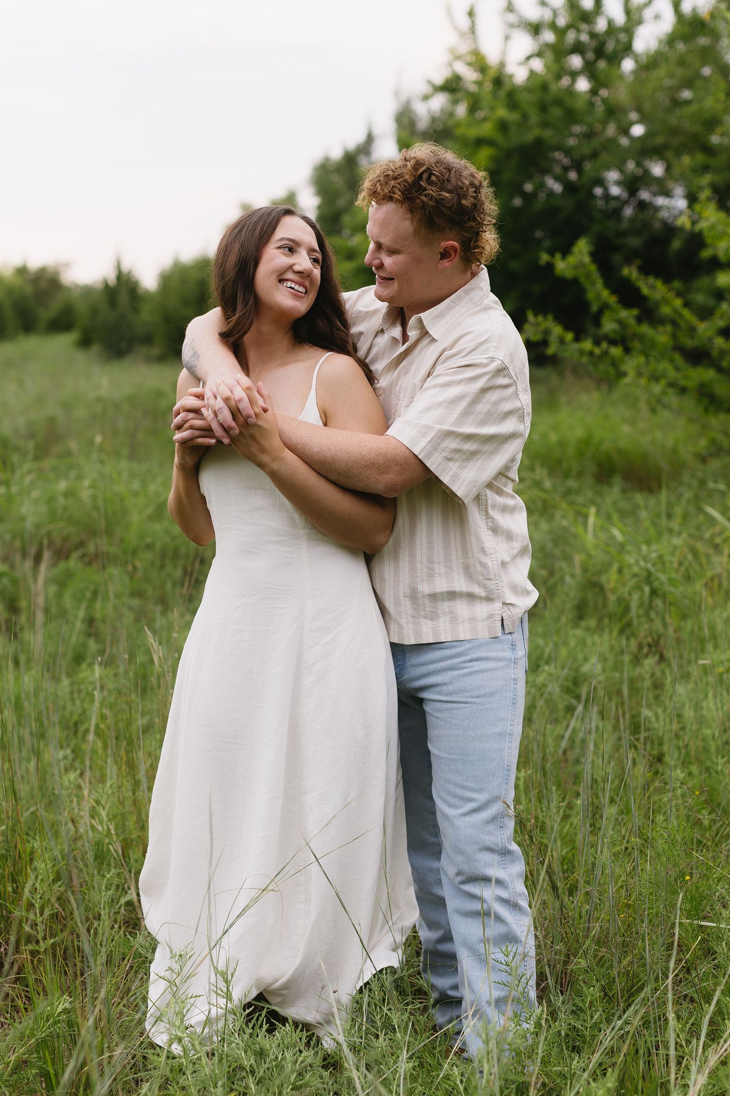 A couple laughs together while embracing in a meadow with tall grass.