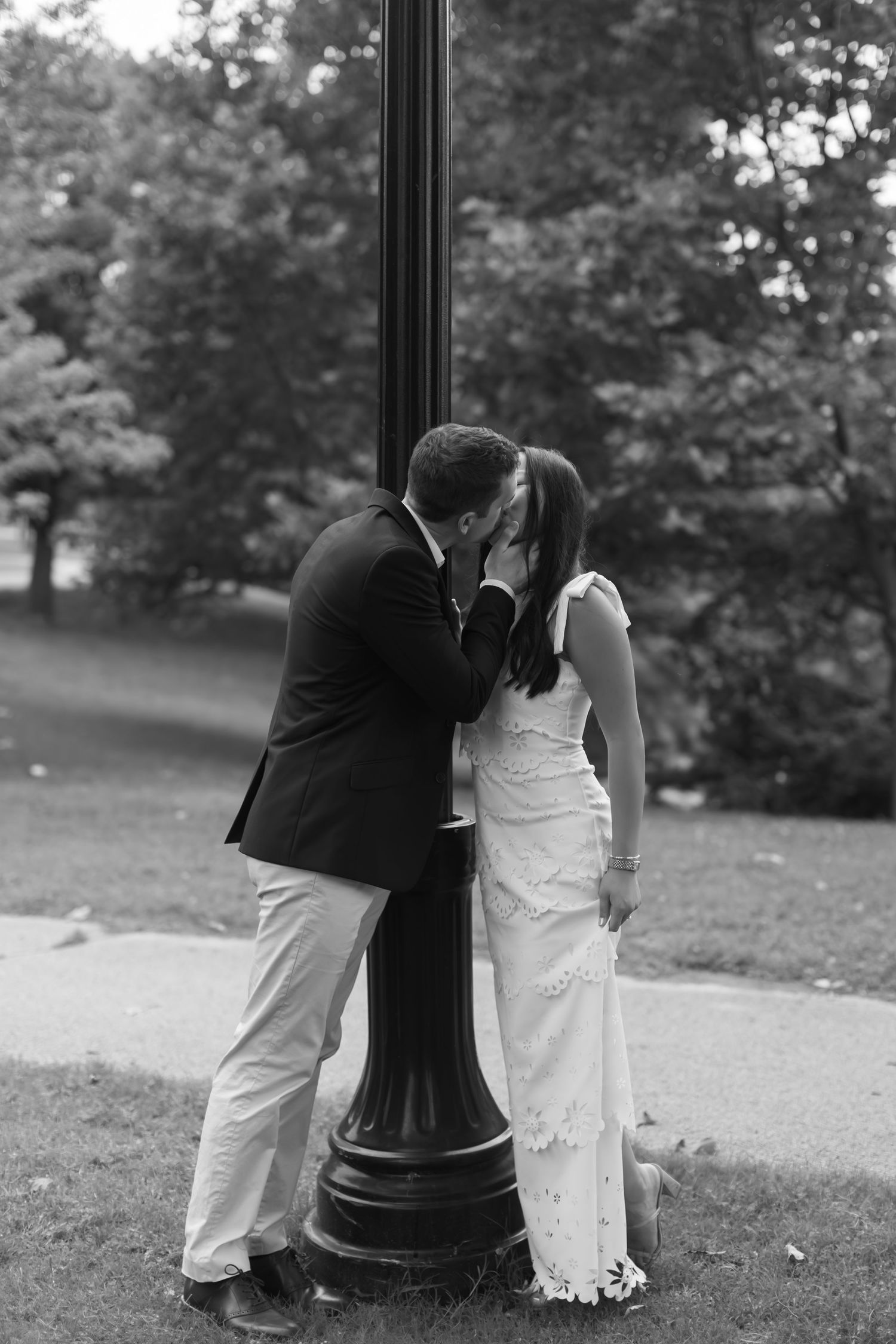 A tender black and white moment shared beside a vintage lamppost in a park setting.