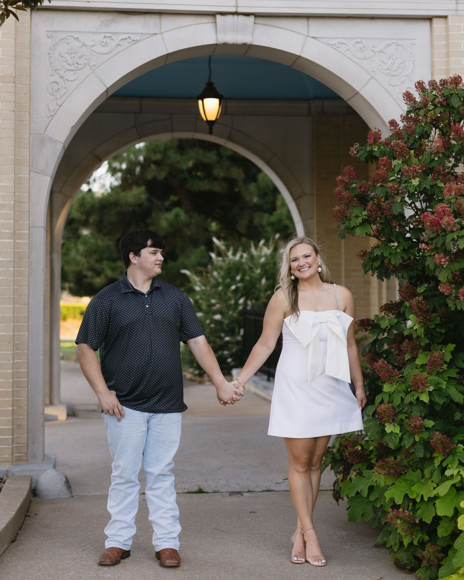 A romantic couple poses beneath ornate archways with climbing roses in an elegant outdoor setting.