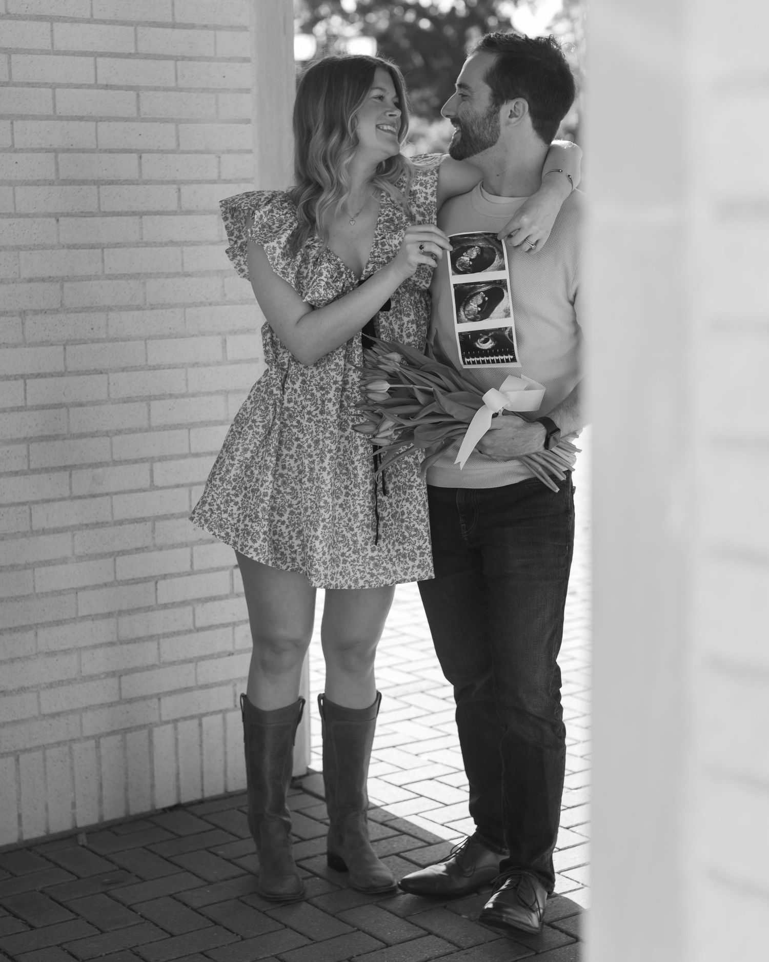 A romantic couple shares five tender moments against a brick wall in a series of black and white photographs.