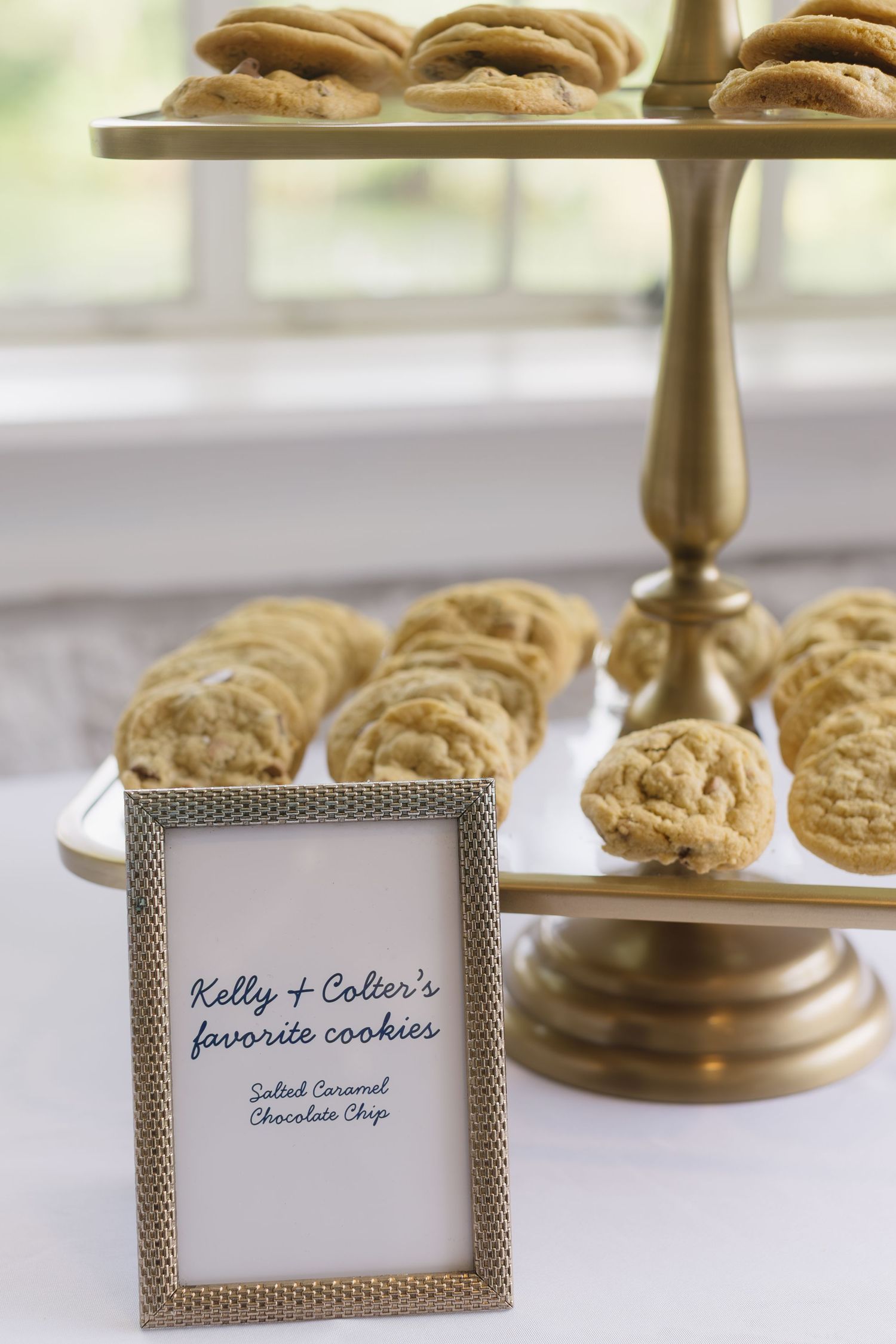 Rustic gold dessert stands displaying cookies with elegant name cards at a wedding reception.