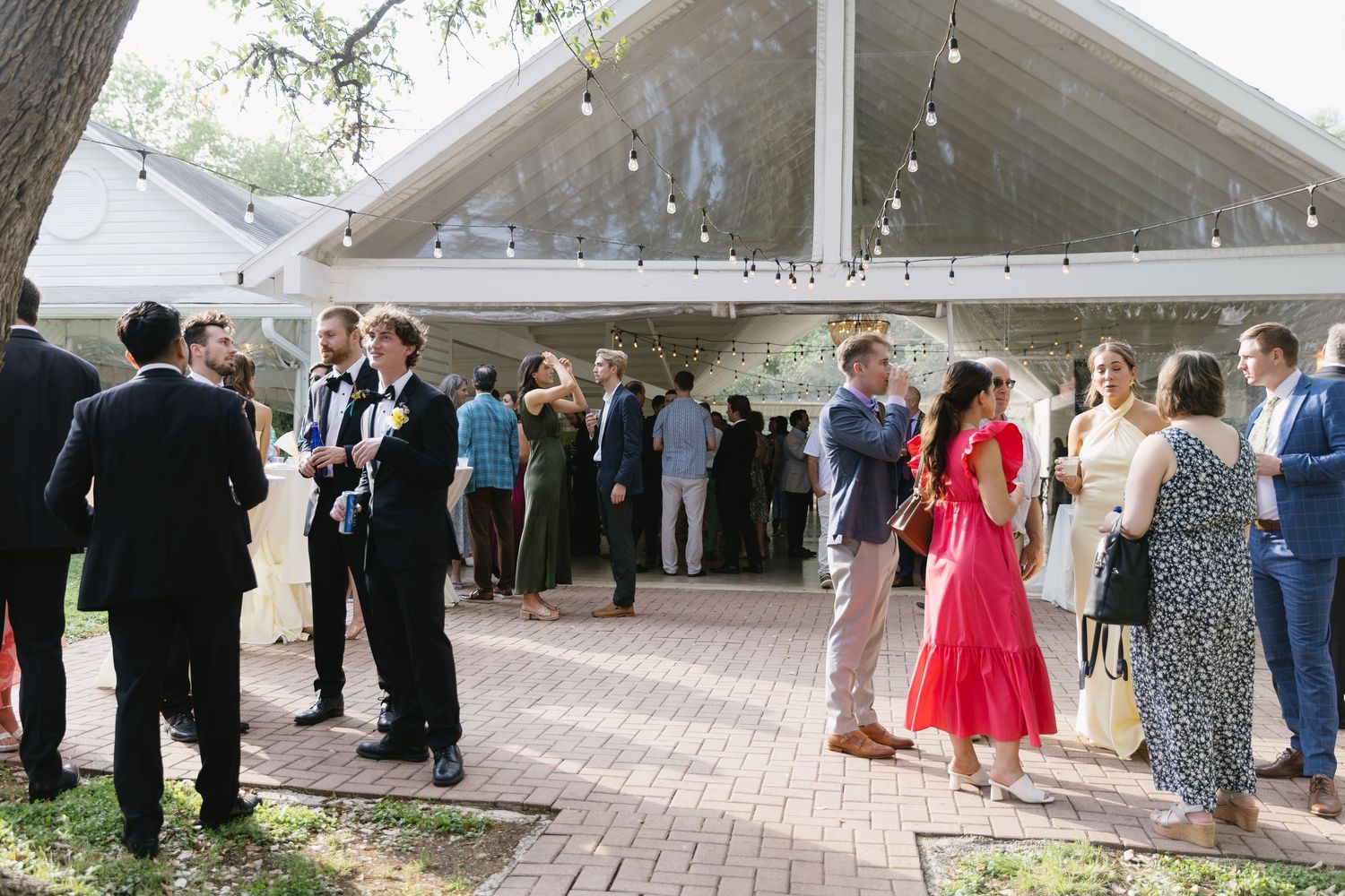 Large wedding reception tent setup with guests mingling on brick patio.