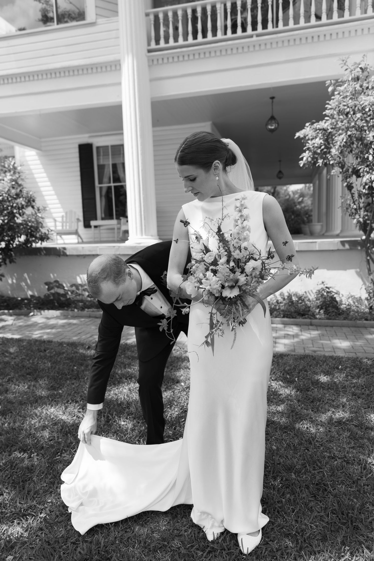 Black and white sequence of a couple in wedding attire leaning over playfully in front of a house with white columns.